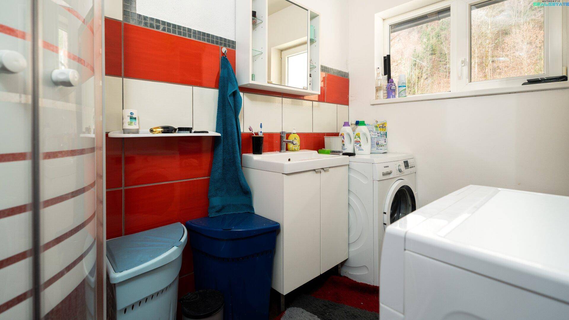 Waschküche mit Waschmaschine, Trockner, Waschbecken und roten Wandfliesen.