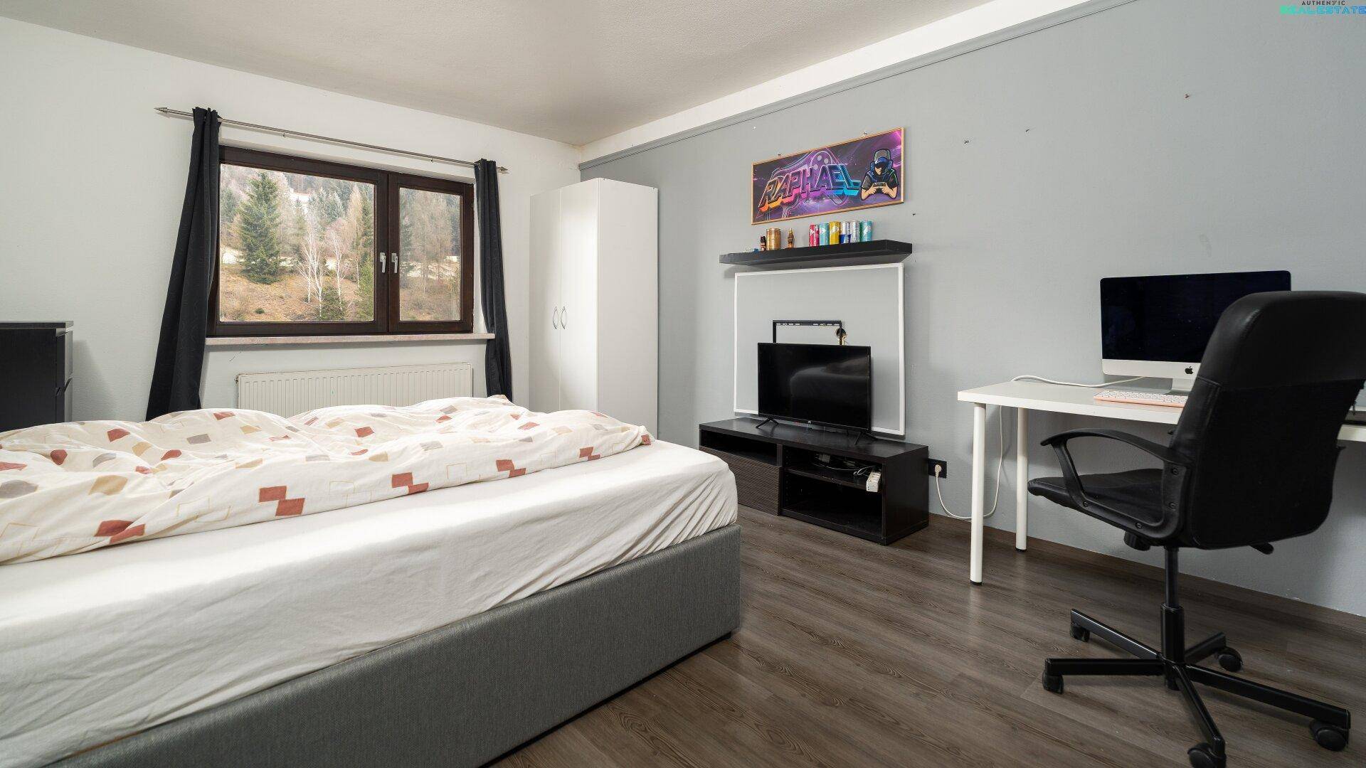 Jugendzimmer mit Bett, Schreibtisch und Blick auf die grüne Landschaft.