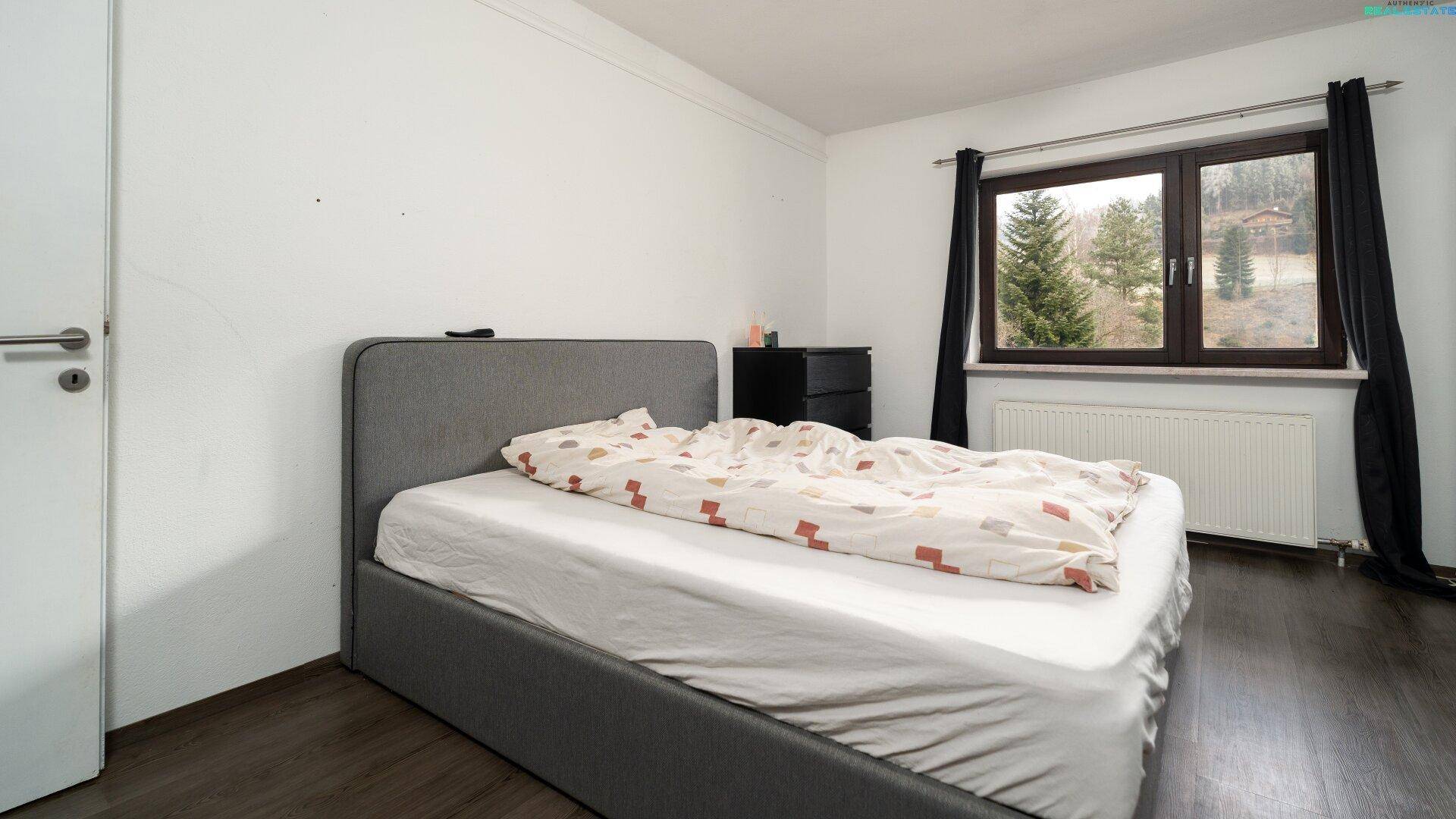Schlafzimmer mit Doppelbett, Fenster und Heizkörper, einfach eingerichtet.