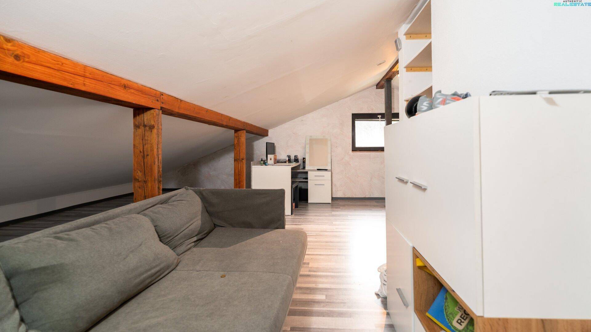Ausgebauter Dachboden mit Sofa, Stauraum und sichtbaren Holzbalken.