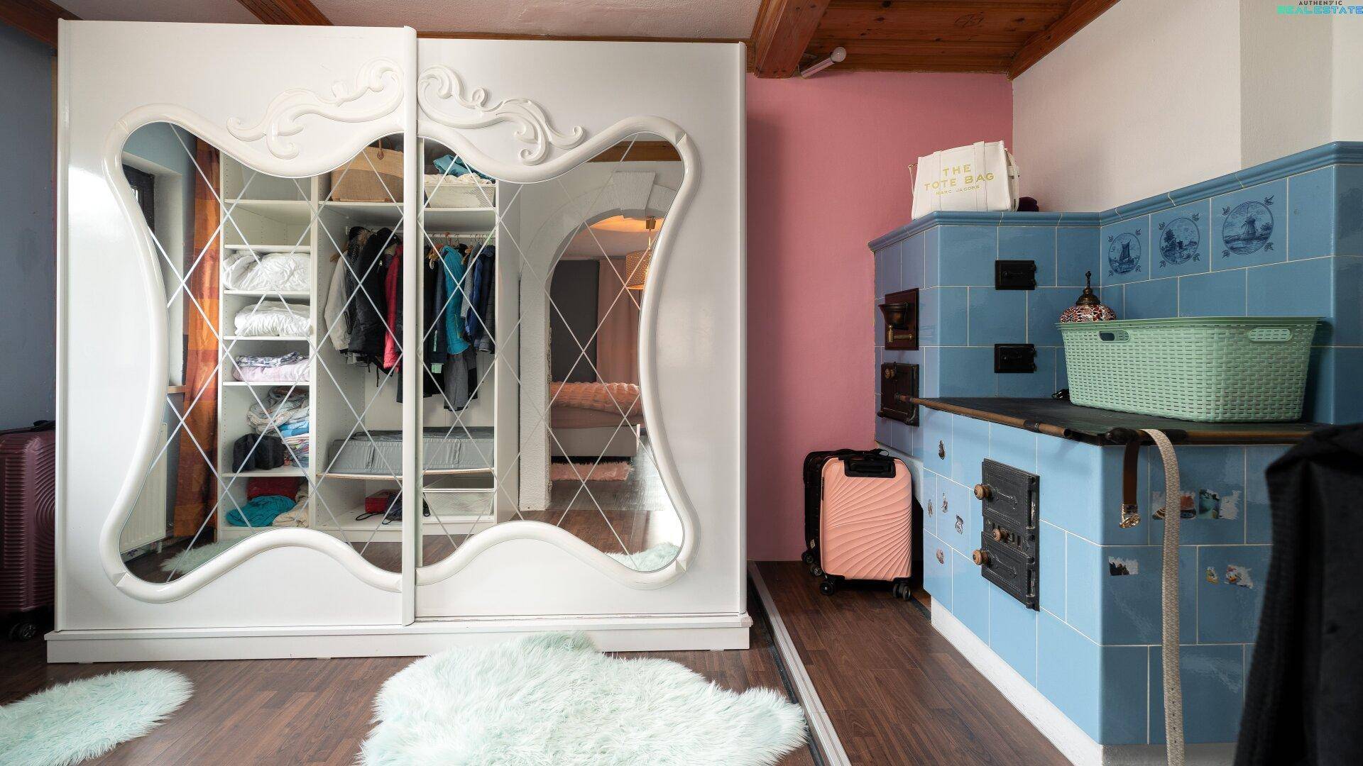 Schlafzimmer mit großem Spiegelschrank, Kachelofen und Holzbalken an der Decke.
