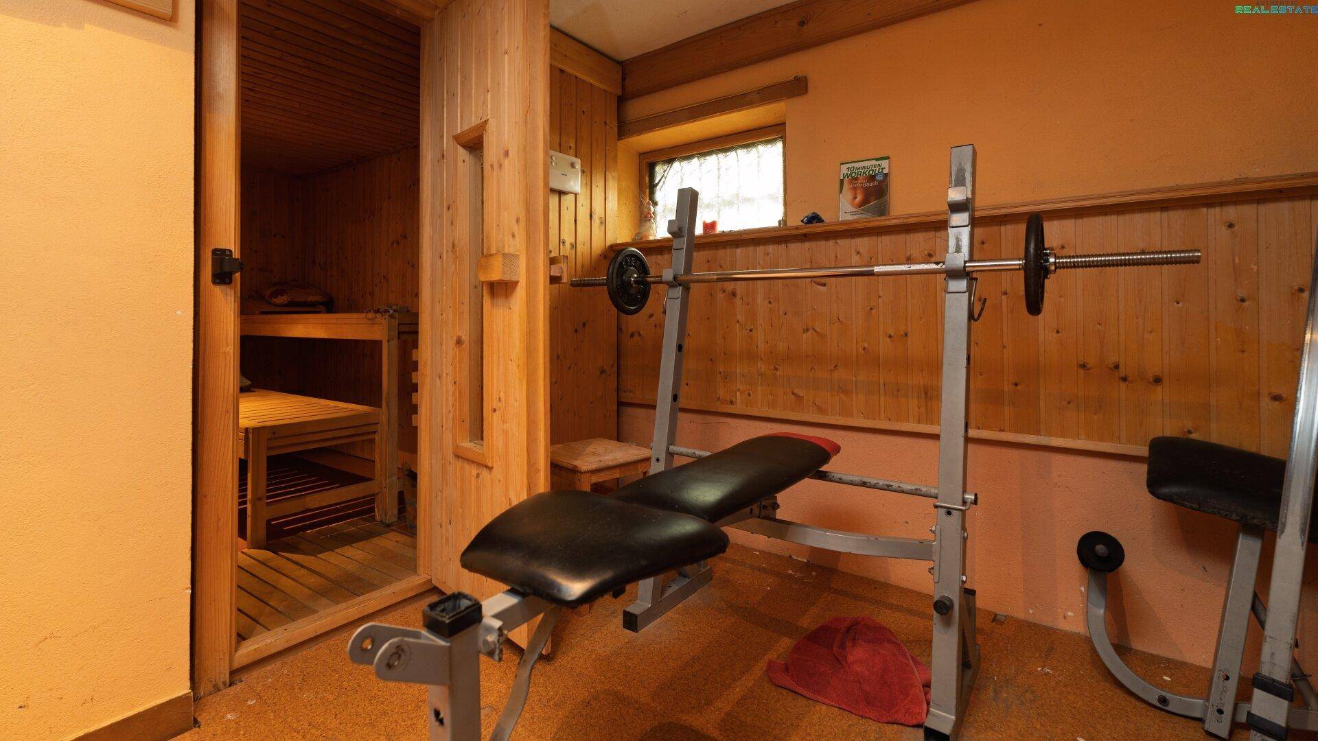Fitnessraum mit Hantelbank und angrenzender Sauna für Wellness.