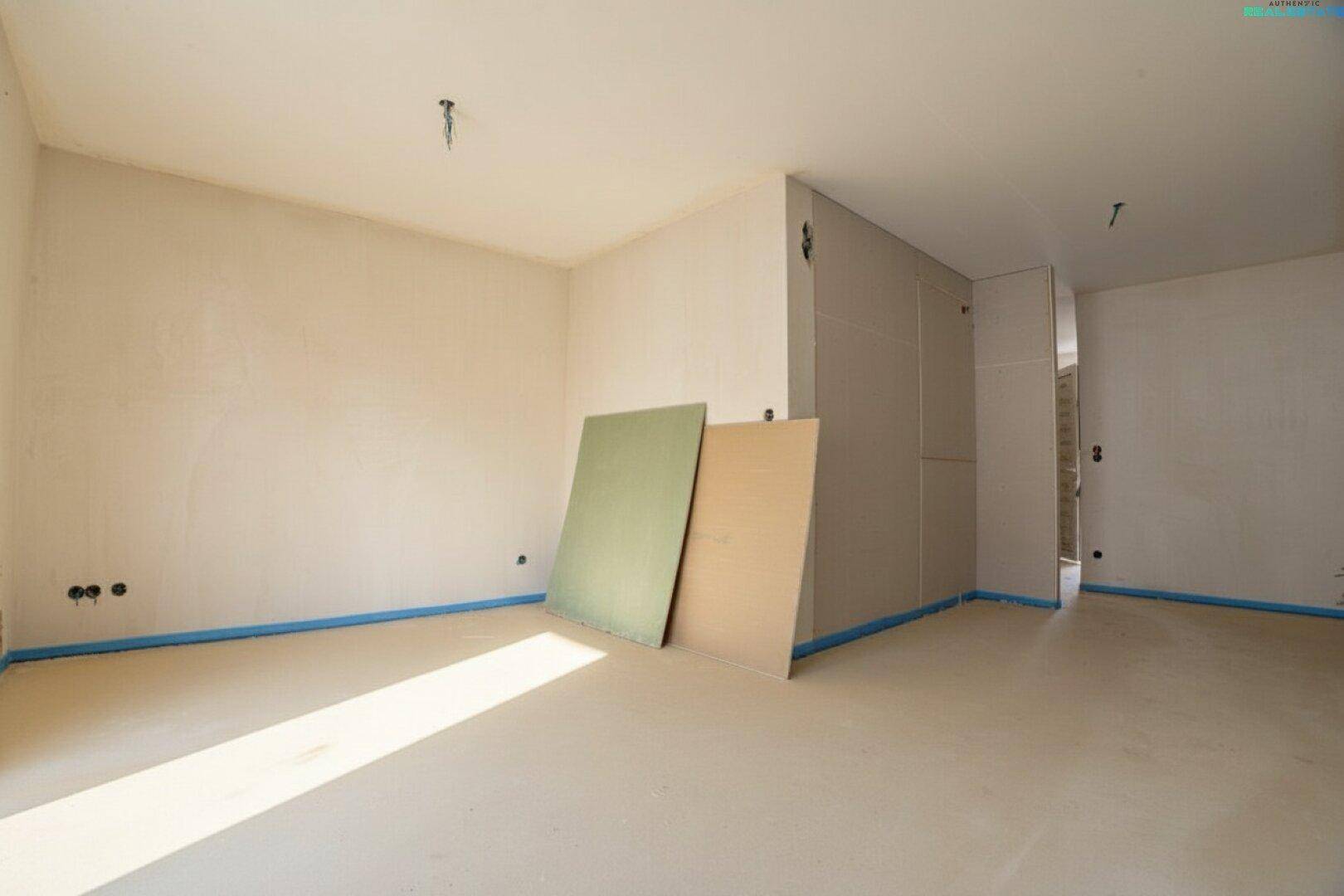 Geräumiger Wohnbereich im Rohbau mit viel Tageslicht und vorbereiteten Wänden für den Ausbau.