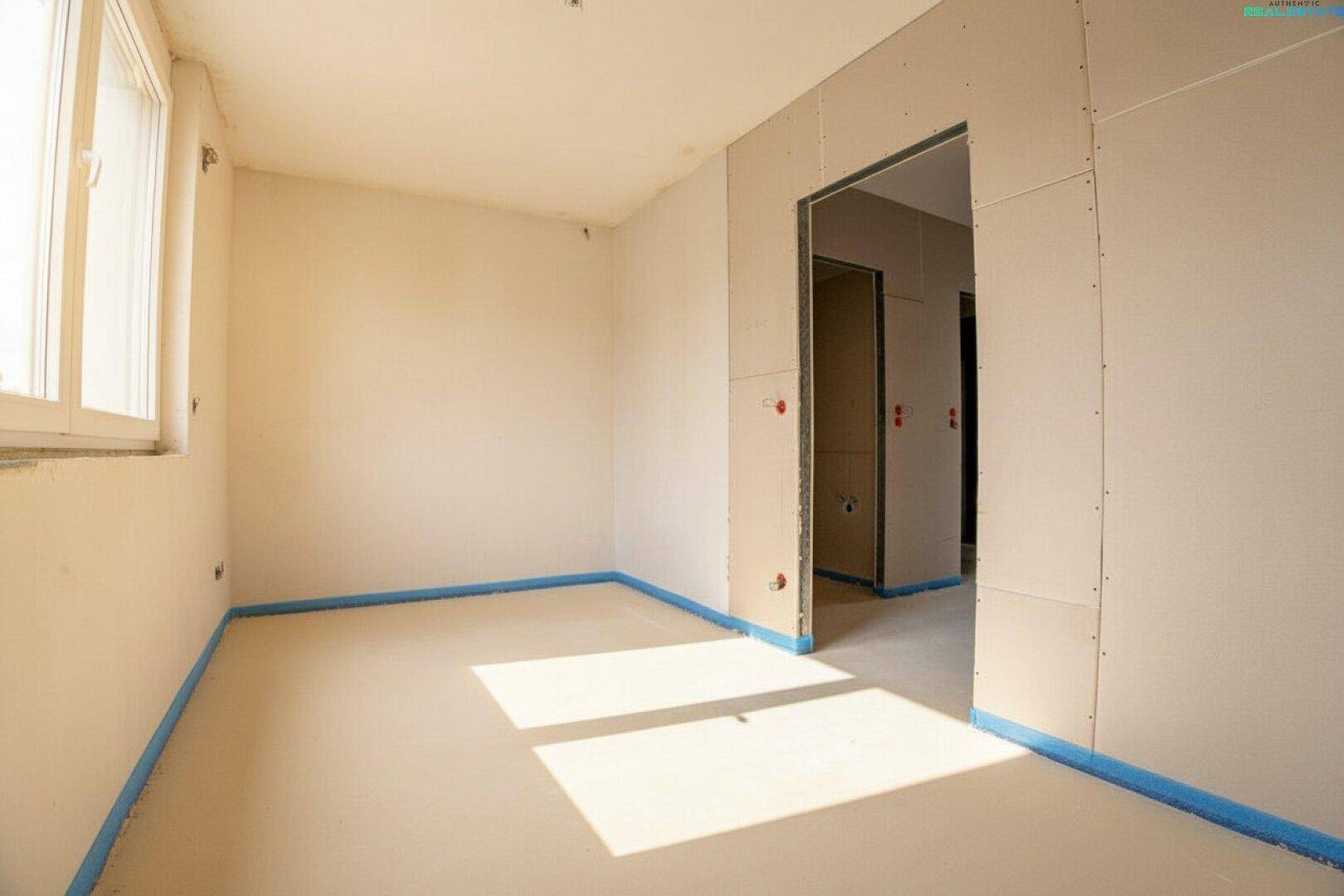 Schlafzimmer im Rohbau mit Fenster und vorbereiteten Wänden für den weiteren Ausbau.