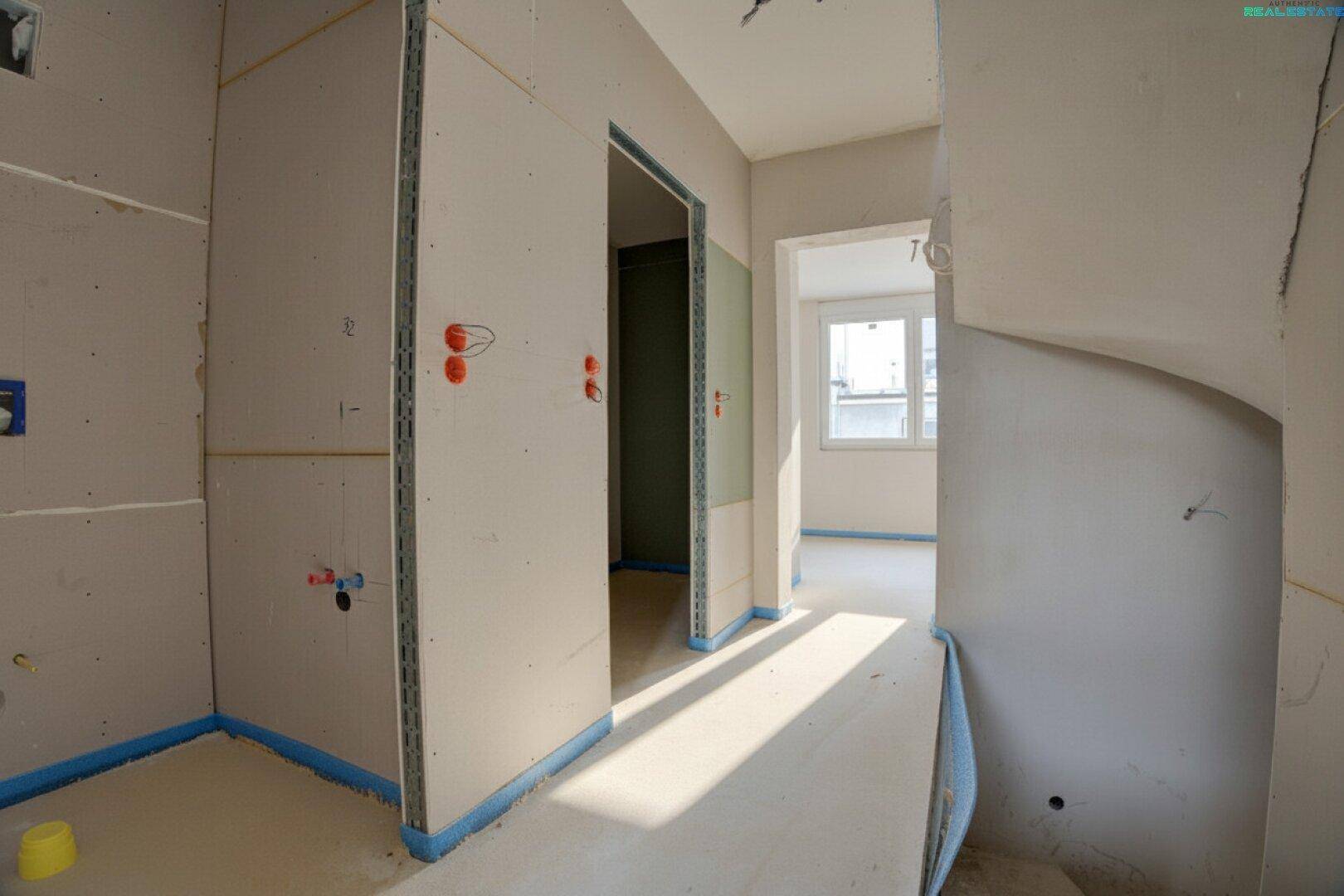 Flurbereich im Rohbau mit mehreren Türöffnungen und sichtbaren Trockenbauarbeiten.