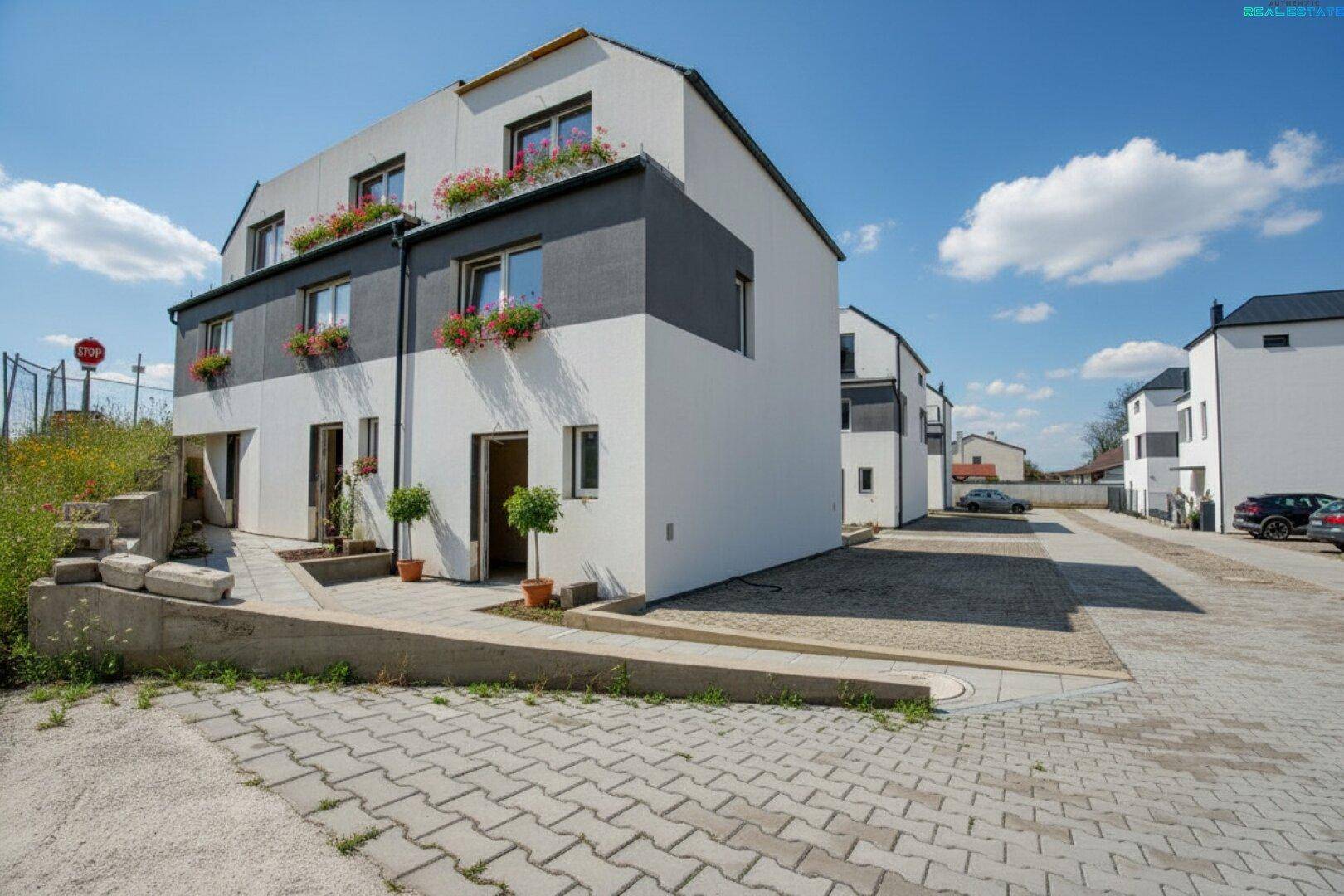 Moderne Reihenhäuser mit weißer und grauer Fassade, Blumenkästen und gepflastertem Zugangsbereich.