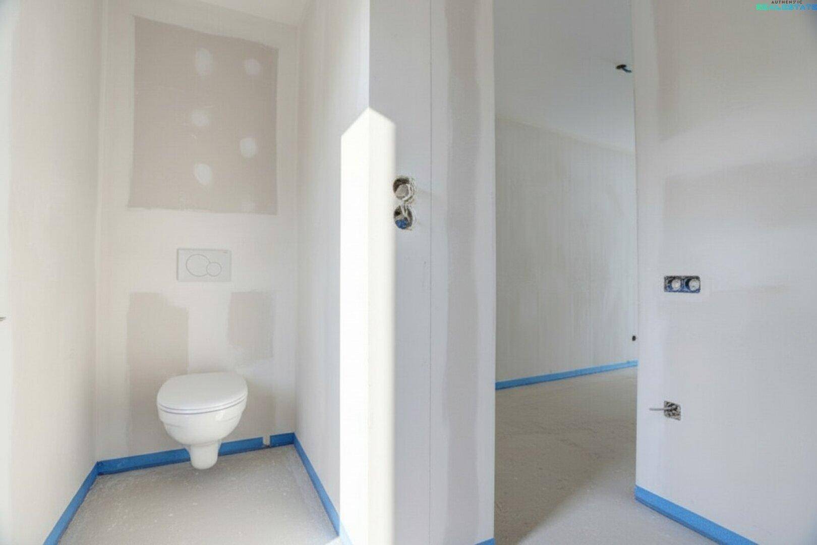 Gäste-WC im Rohbau mit installierter Wandtoilette und vorbereiteten Wänden.