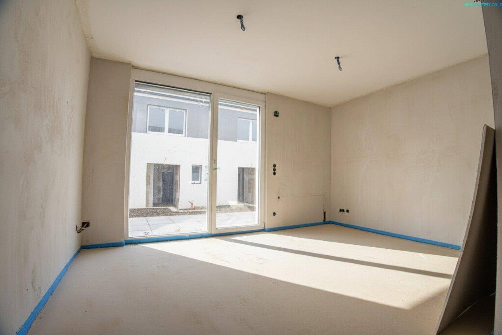 Heller Wohnraum im Rohbau mit großer Schiebetür und Blick auf den Außenbereich.