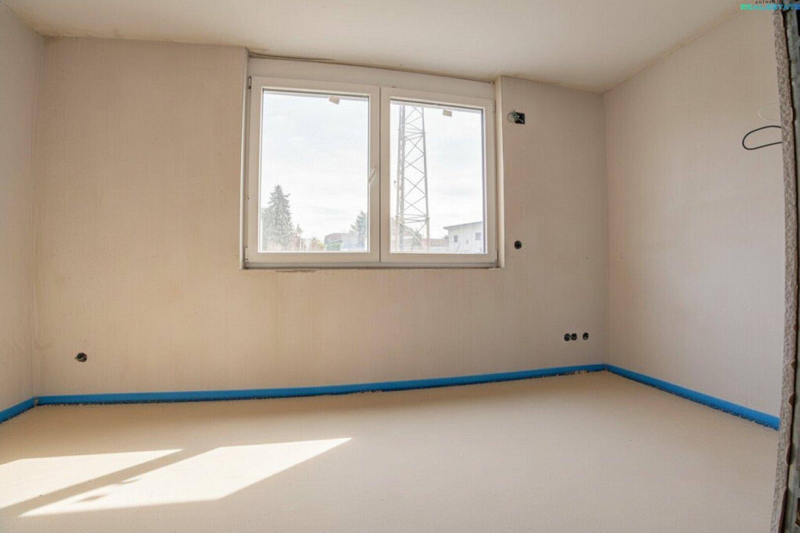 Schlafzimmer im Rohbau mit großem Fenster und viel Tageslicht.
