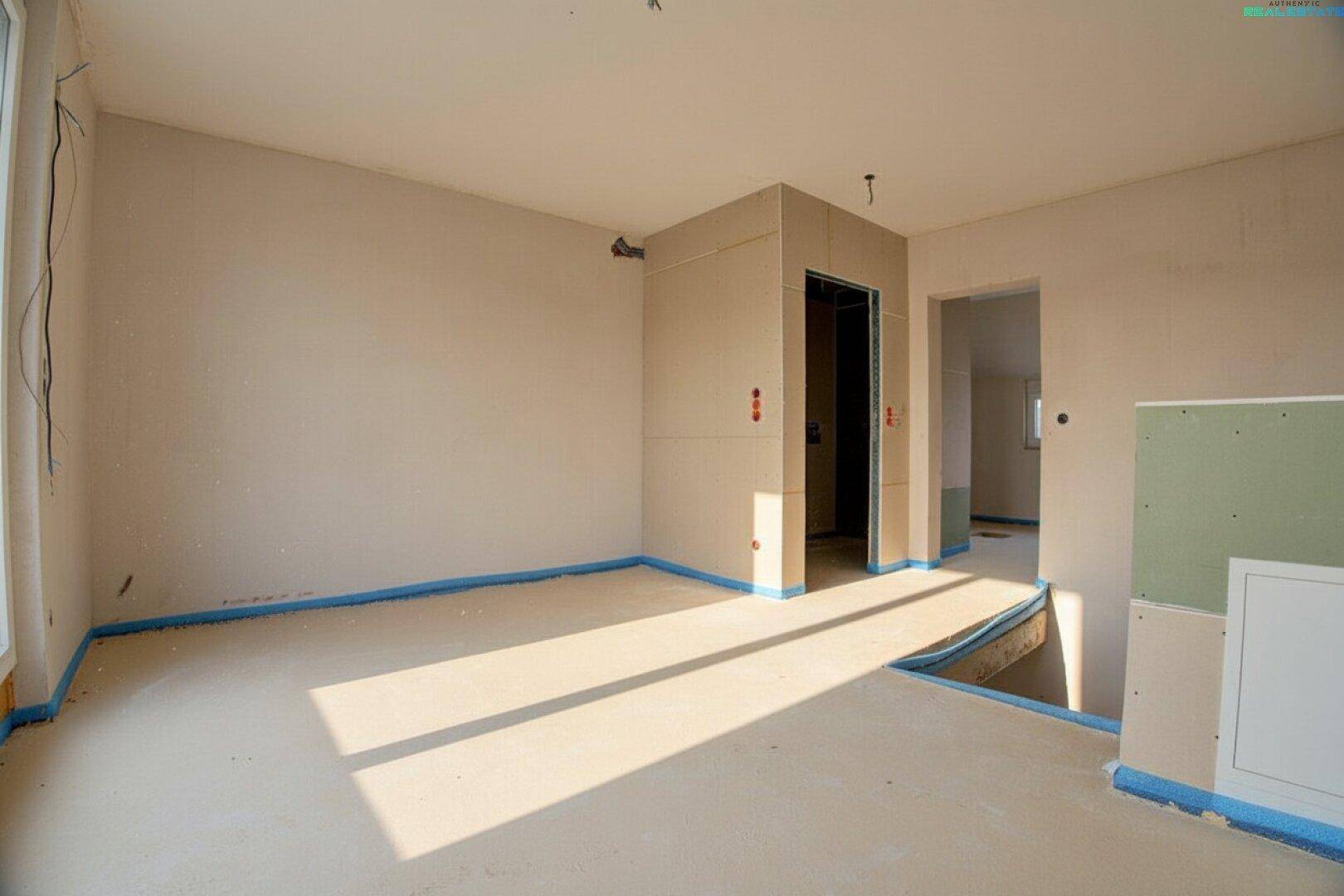 Heller Raum im Rohbau mit Estrichboden und vorbereitetem Aufzugschacht.