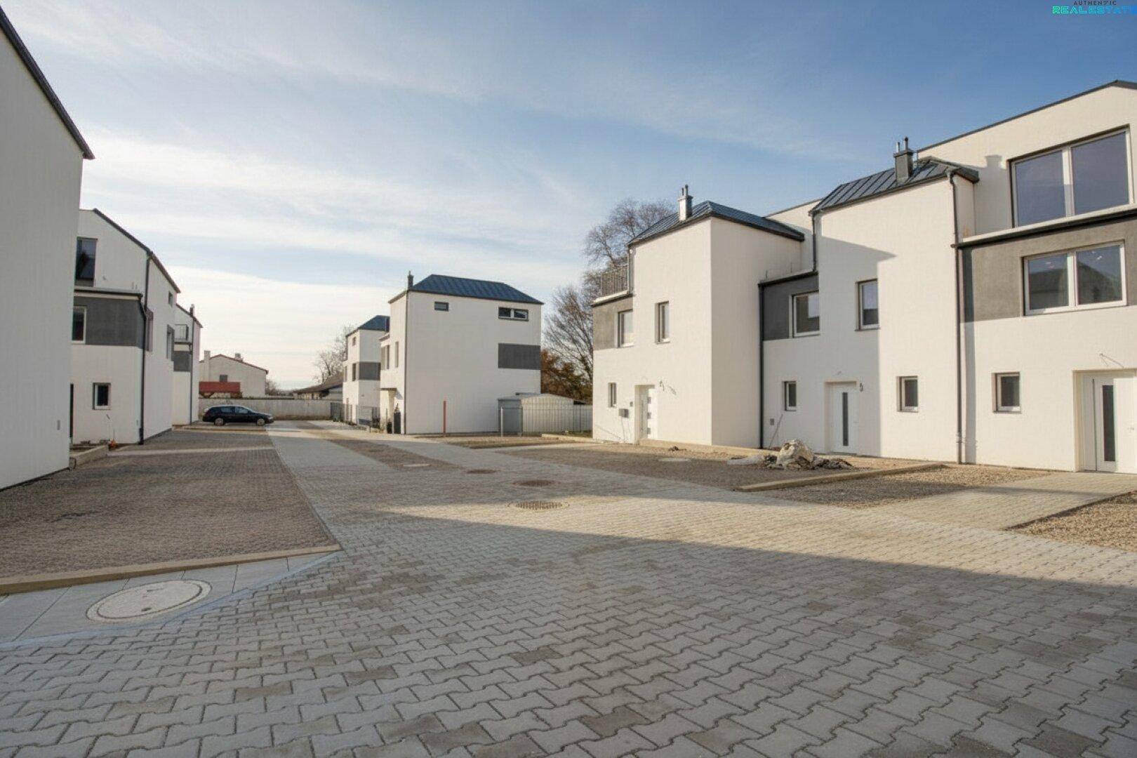 Reihenhaussiedlung mit modernen Gebäuden, gepflasterten Wegen und Parkplätzen.