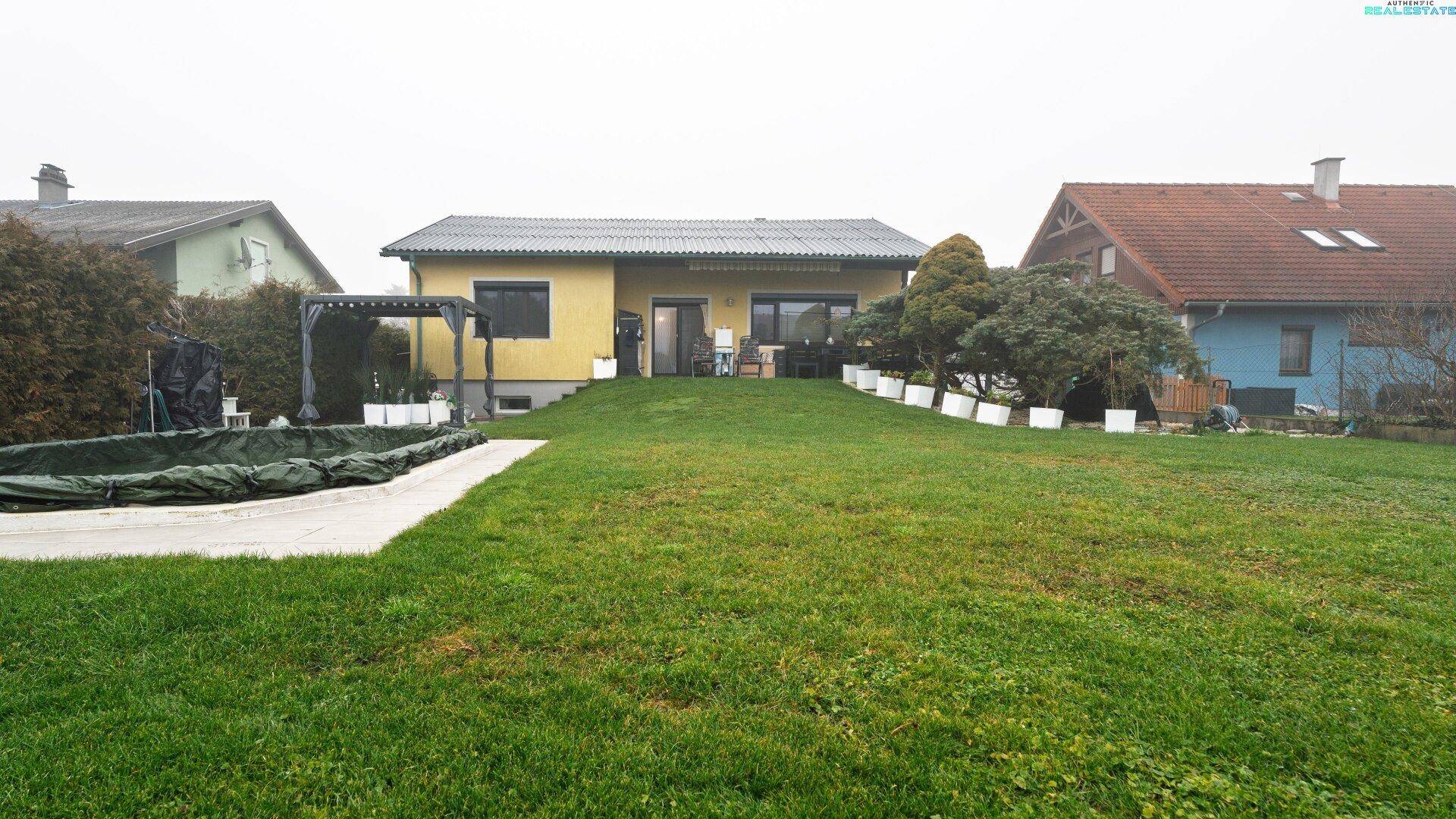 Blick vom Garten auf die Rückseite des Hauses mit Terrasse und Rasenfläche.