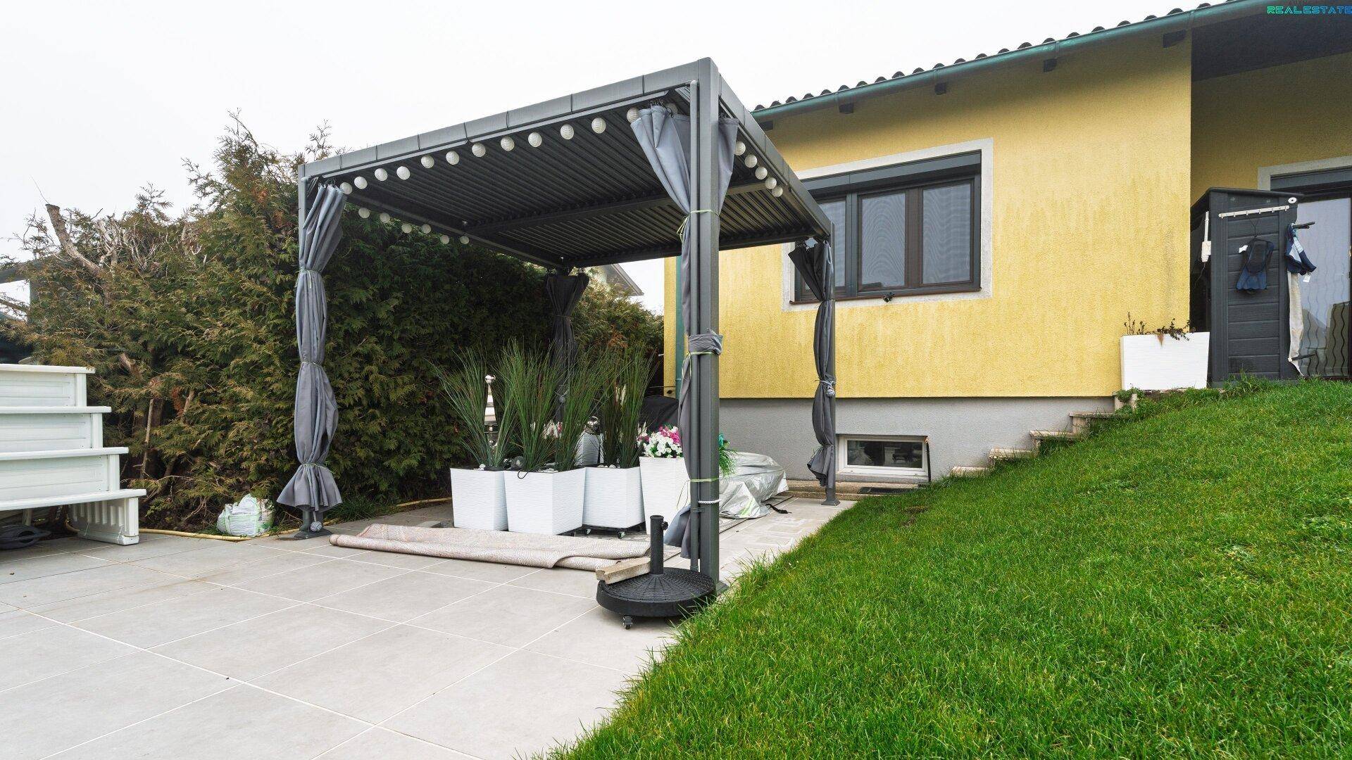 Gepflasterte Terrasse mit moderner Pergola und Sitzgelegenheiten im Freien.
