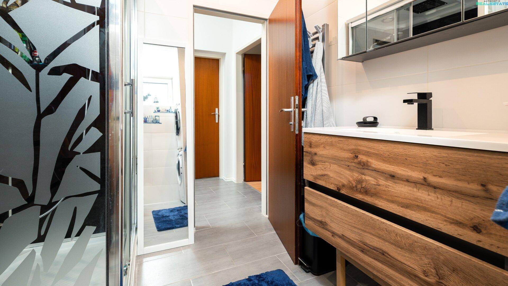 Badezimmer mit moderner Duschkabine und Holzwaschtisch.