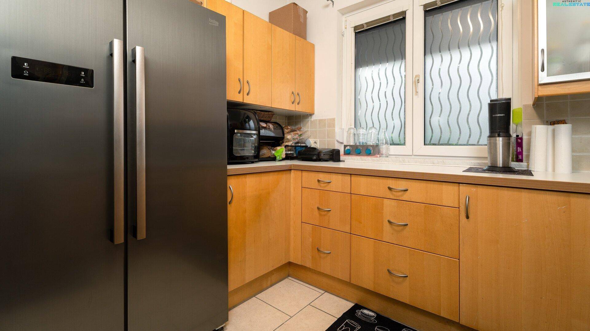 Küche mit großem Kühlschrank, Holzschränken und Fenster.