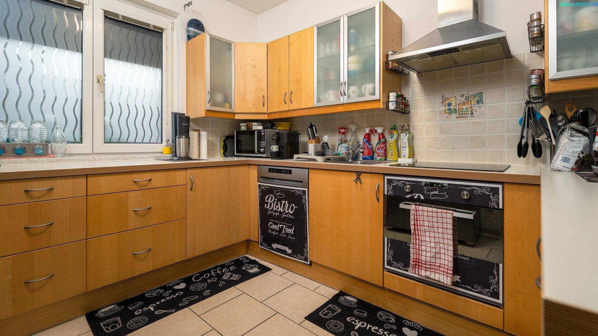 Funktionale Küche mit Holzschränken, Fliesenboden und allen notwendigen Geräten.