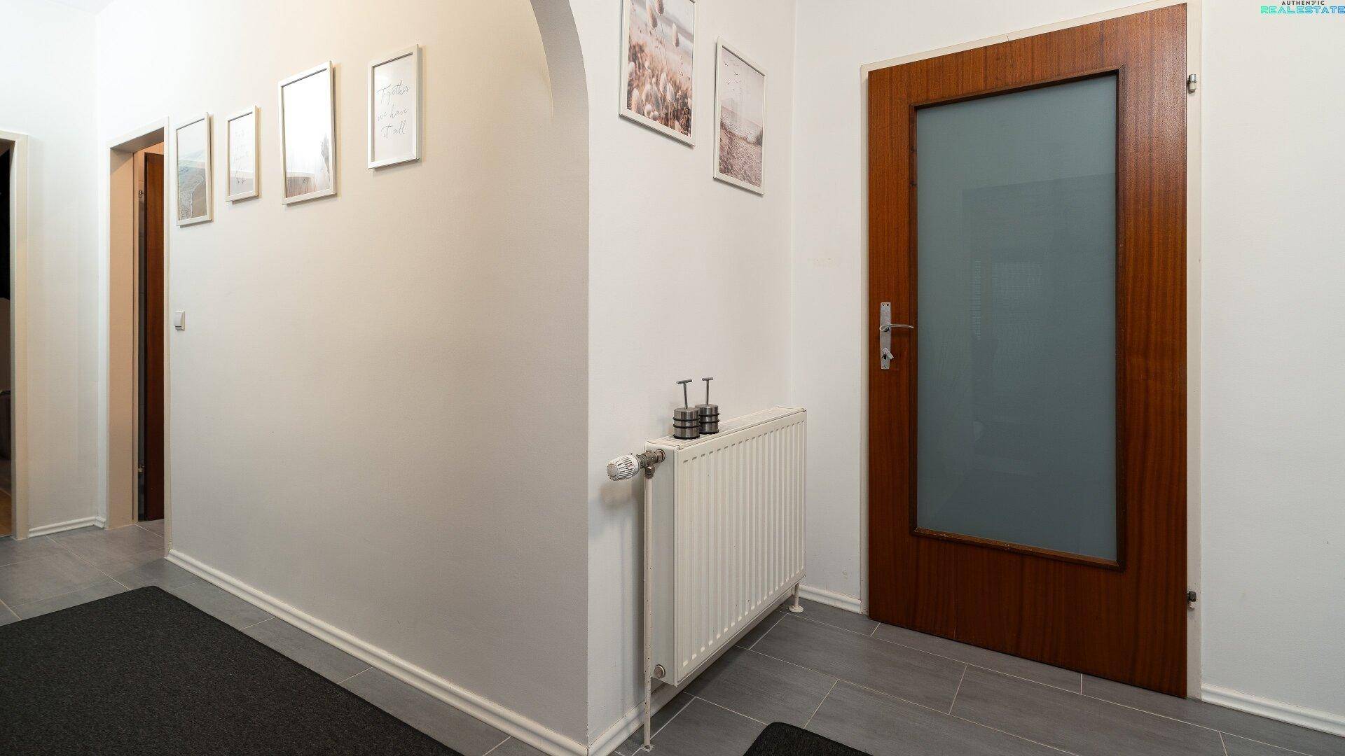 Heller Flur mit Fliesenboden und einer Holztür mit Glaseinsatz.