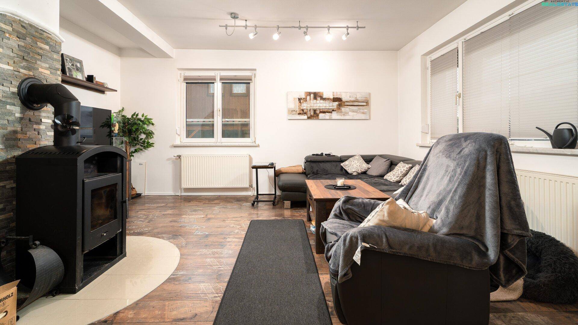 Helles Wohnzimmer mit Kaminofen, Holzboden und großem Sofa.