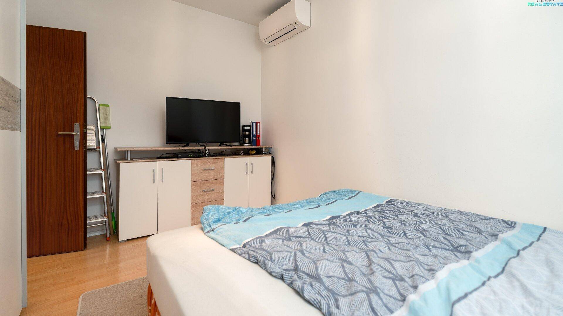 Schlafzimmer mit Fernseher, Holzboden und Zugang zu weiteren Räumen.