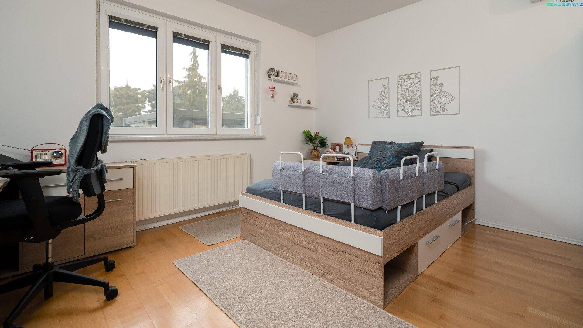 Helles Schlafzimmer mit Holzboden, großem Fenster und Arbeitsbereich.