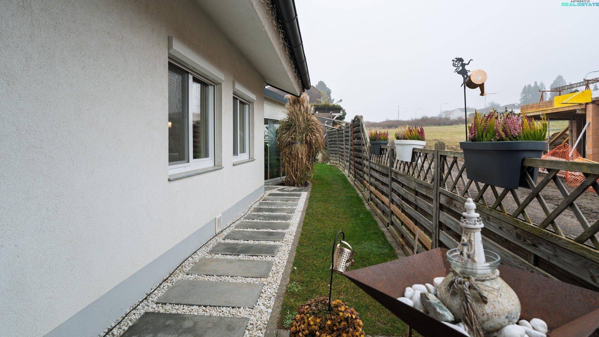 Seitenansicht des Hauses mit einem gepflasterten Gartenweg, Rasenfläche und Holzzaun.