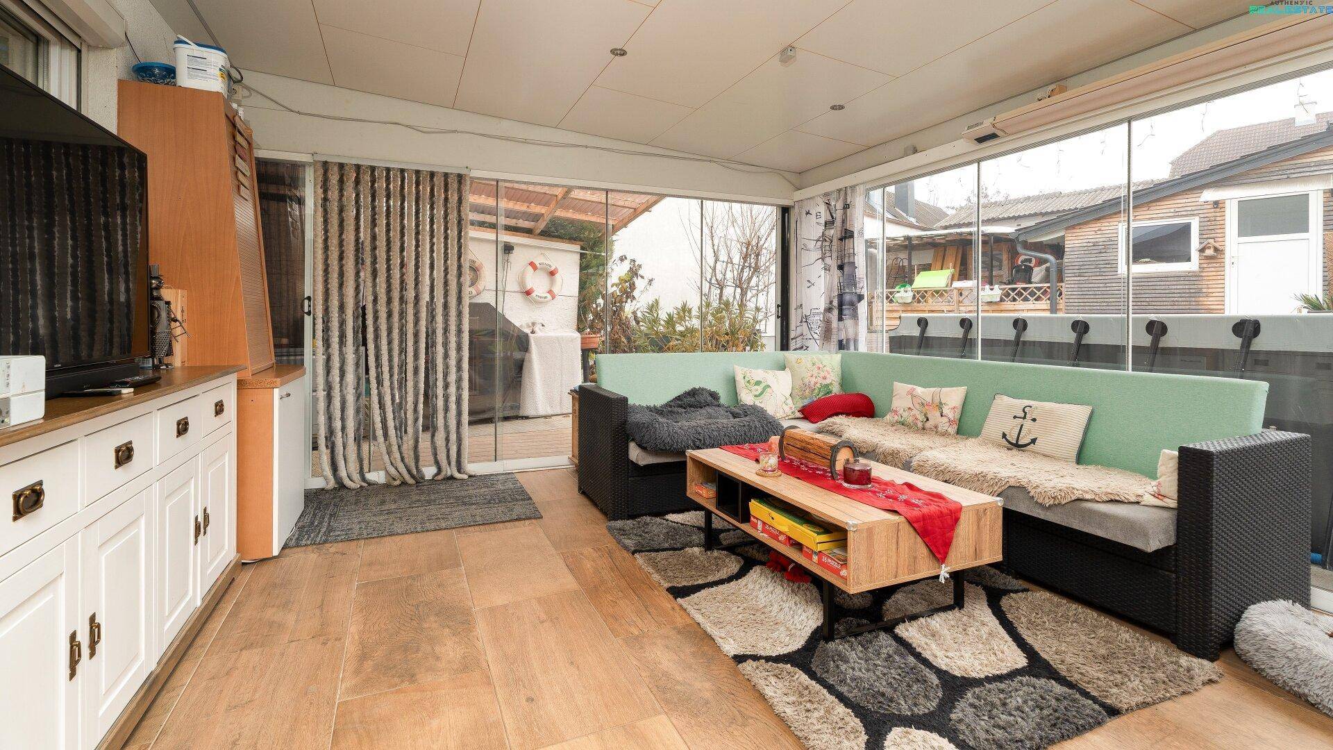 Heller Wintergarten mit Glasfronten, Sitzgelegenheiten und Blick in den Garten.