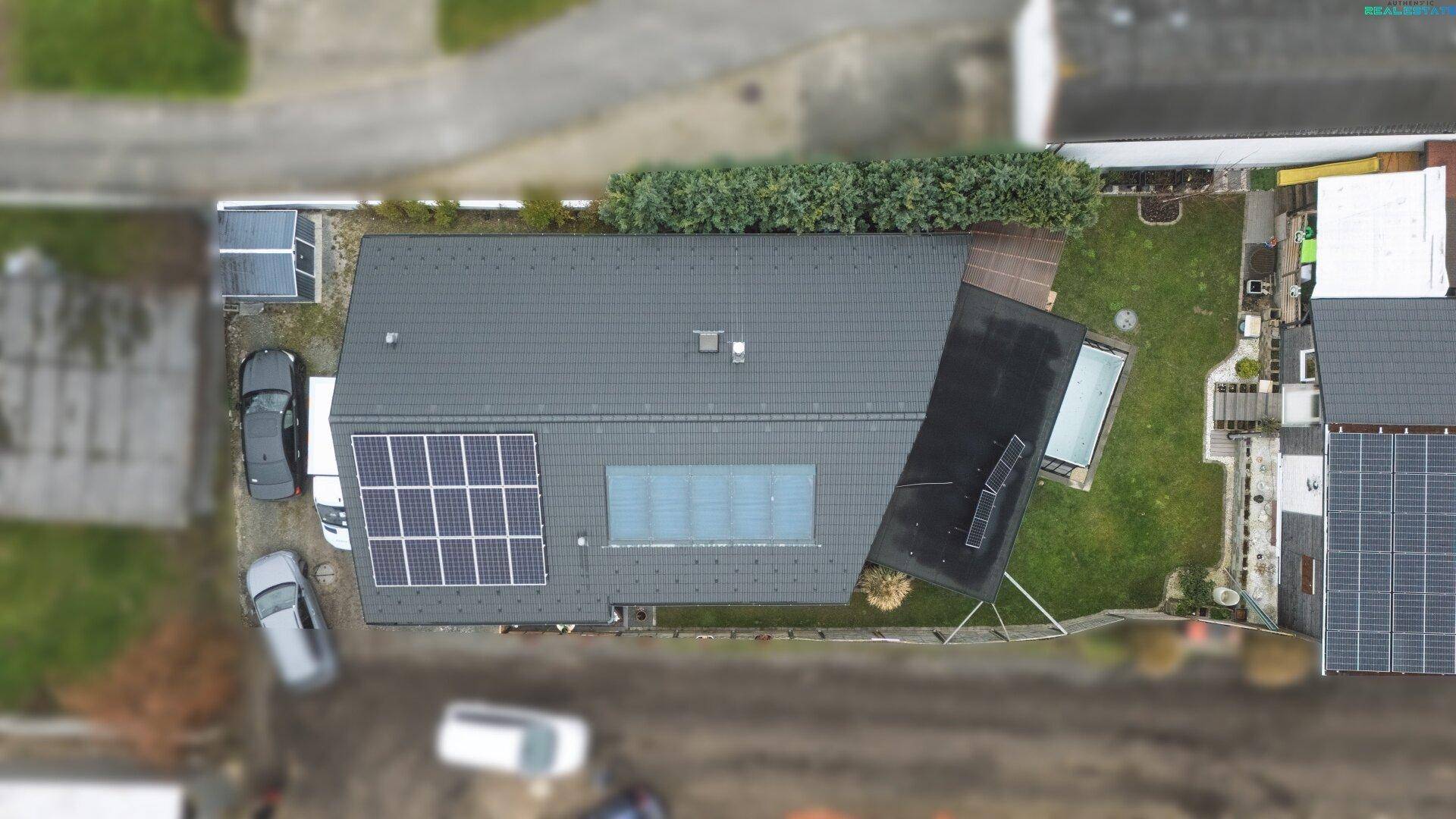 Luftaufnahme eines Einfamilienhauses mit Solaranlage auf dem Dach und Gartenbereich.