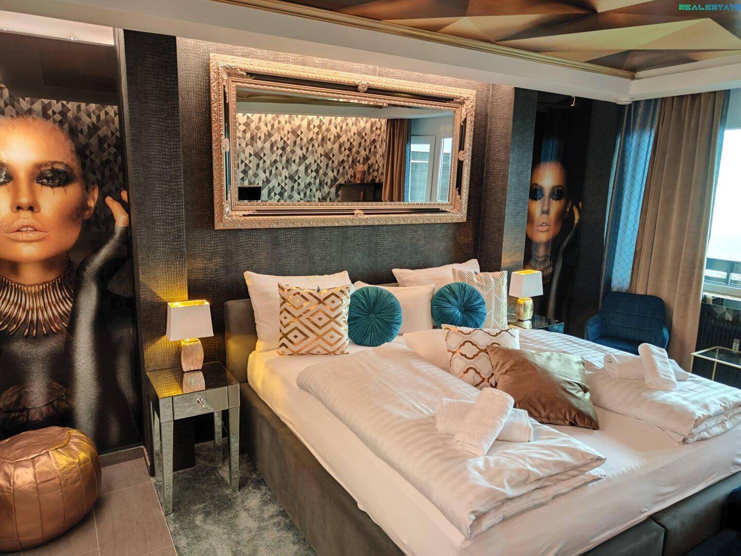 Luxuriöses Schlafzimmer mit großem Doppelbett, opulentem Spiegel und künstlerischen Wanddekorationen.