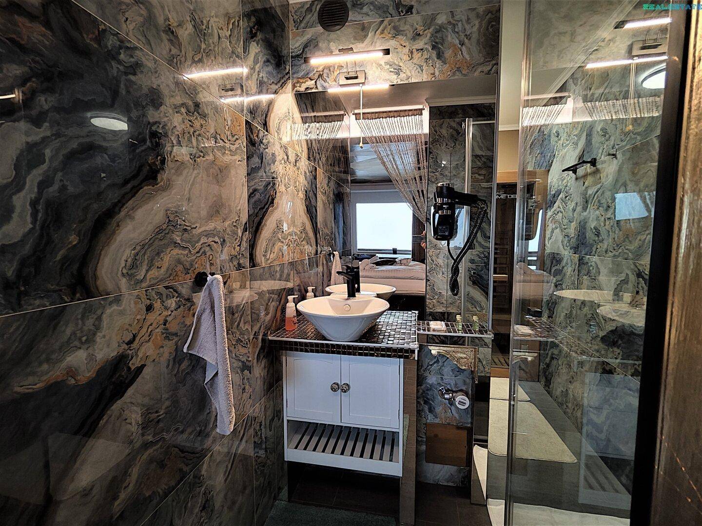 Elegantes Badezimmer mit modernem Waschbecken, großem Spiegel und luxuriösen Marmorfliesen.