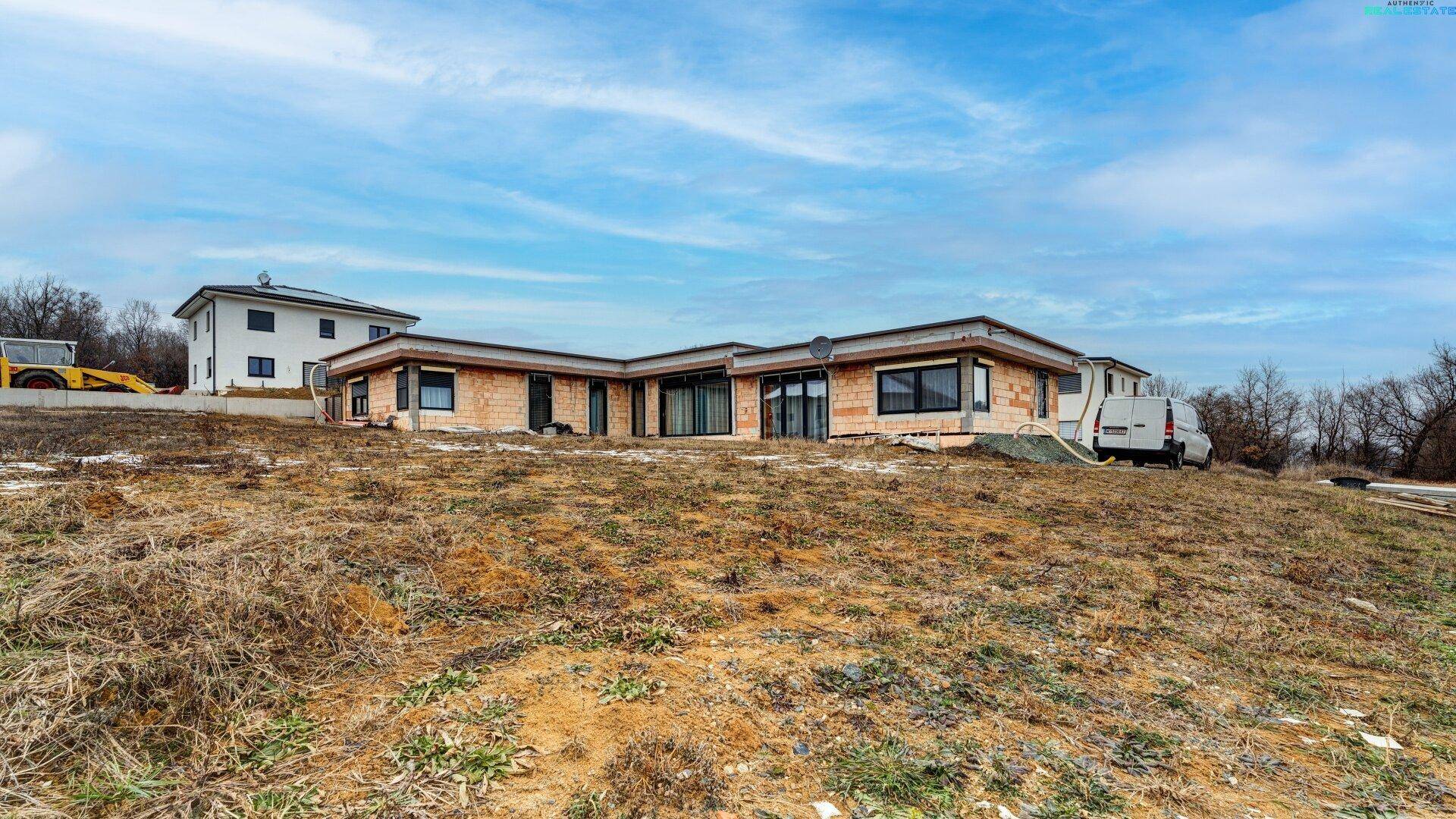 Modernes Einfamilienhaus in Bauphase mit umliegendem Grundstück und Baustellenfahrzeug.