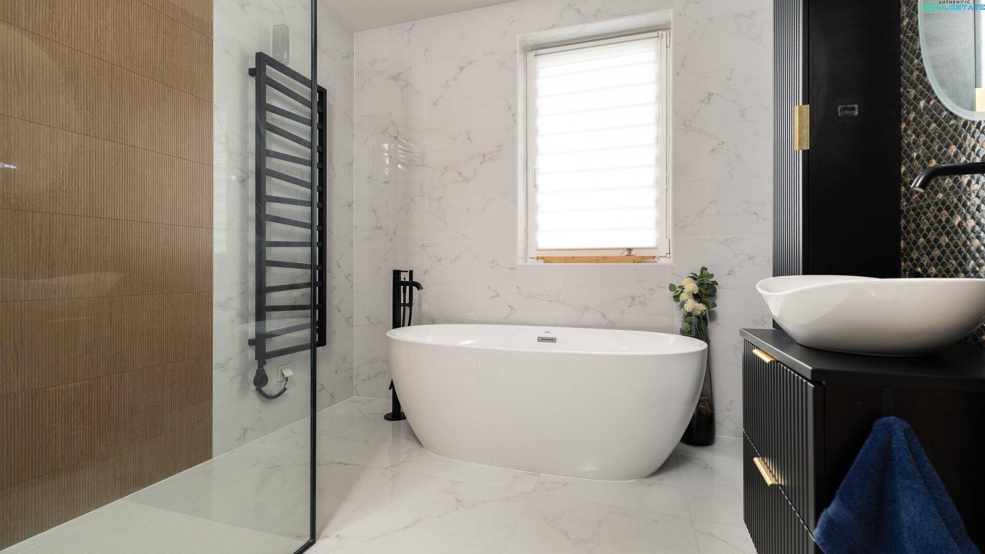 Modernes Badezimmer mit freistehender Badewanne, Dusche und beheiztem Handtuchhalter, luxuriös und funktional.