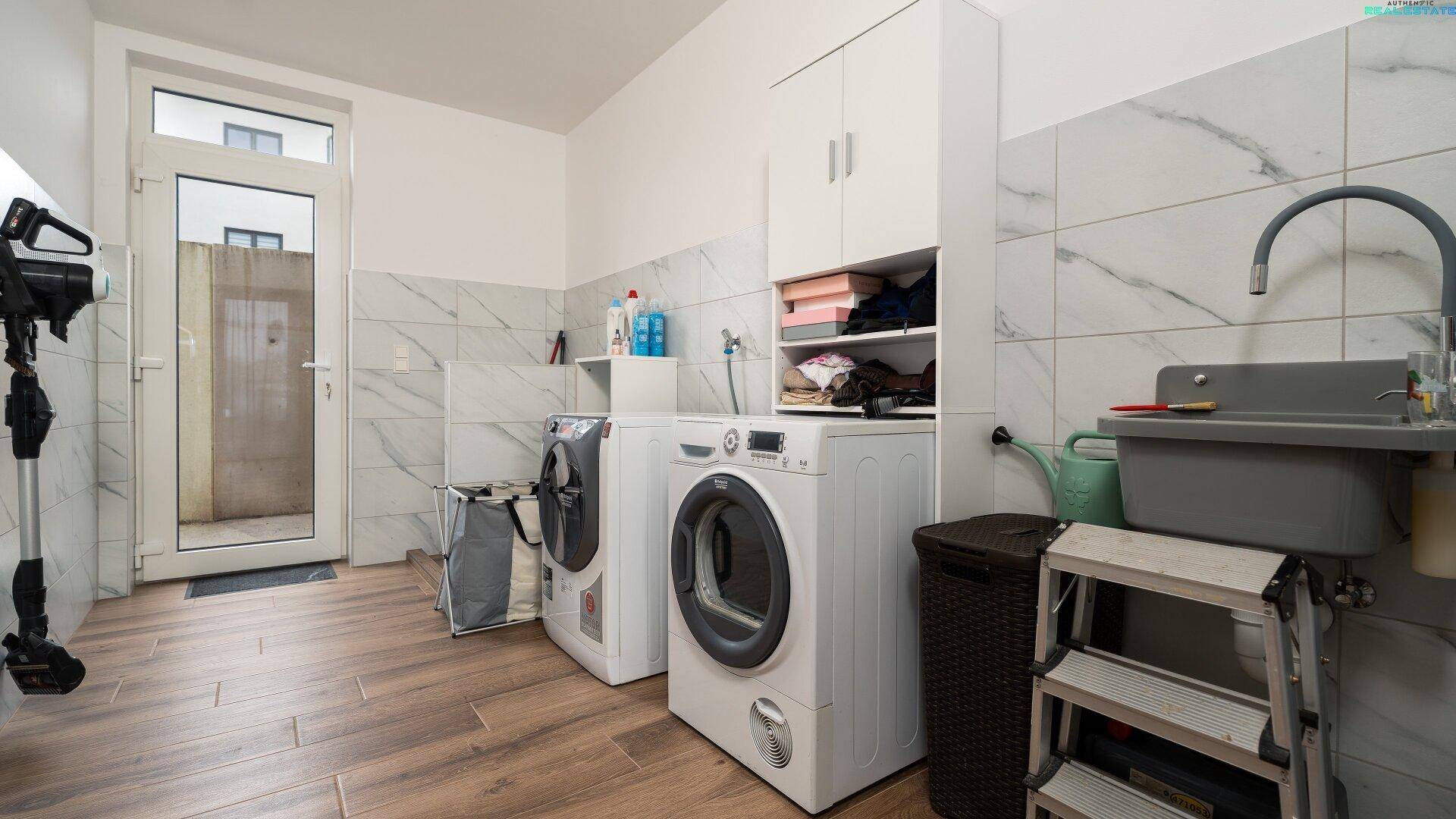 Praktischer Hauswirtschaftsraum mit Waschmaschine, Trockner und Waschbecken, bietet viel Stauraum.