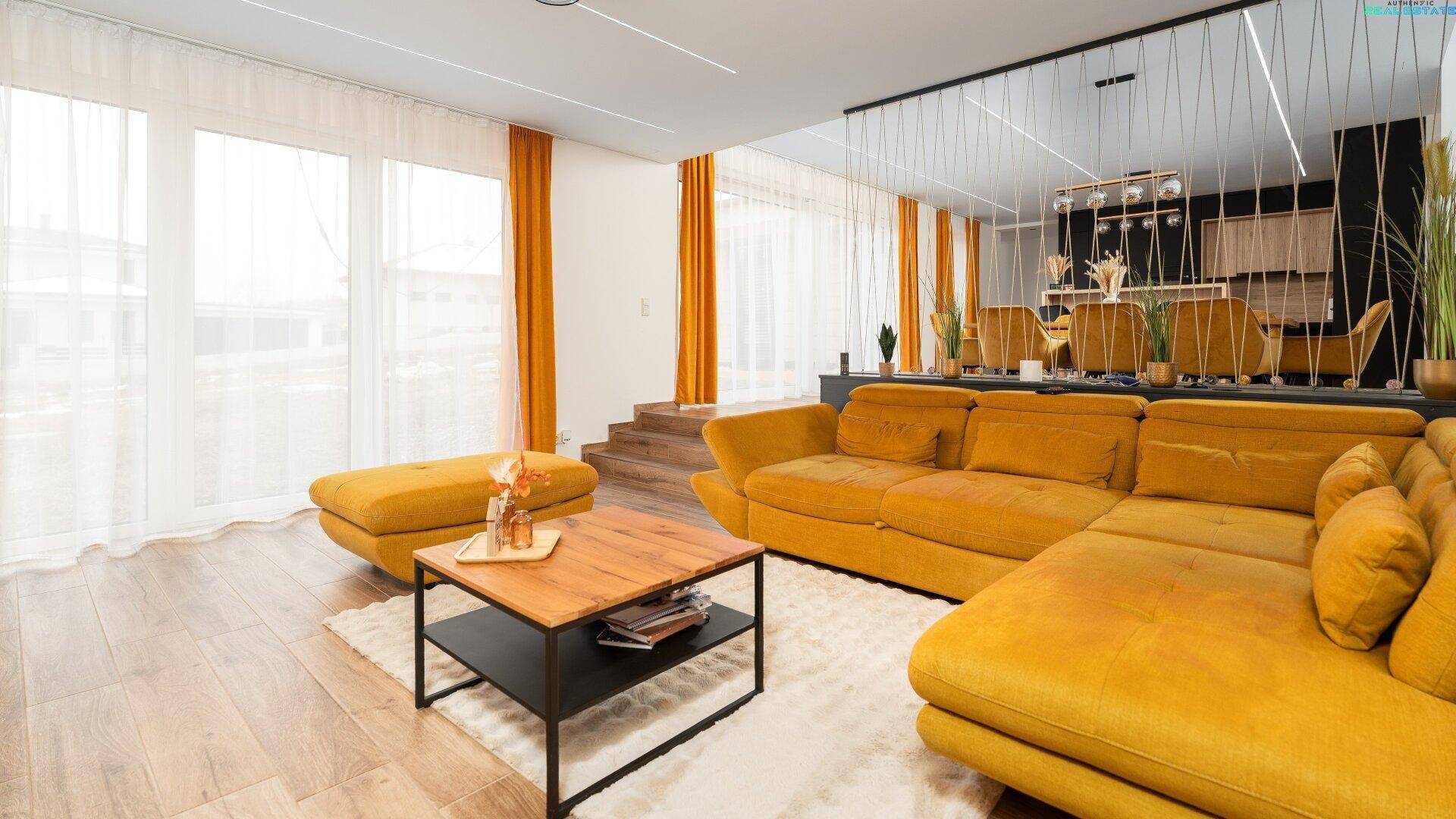 Helles, modernes Wohnzimmer mit gelbem Sofa, Holzboden und großen Fenstern, offen zum Essbereich.