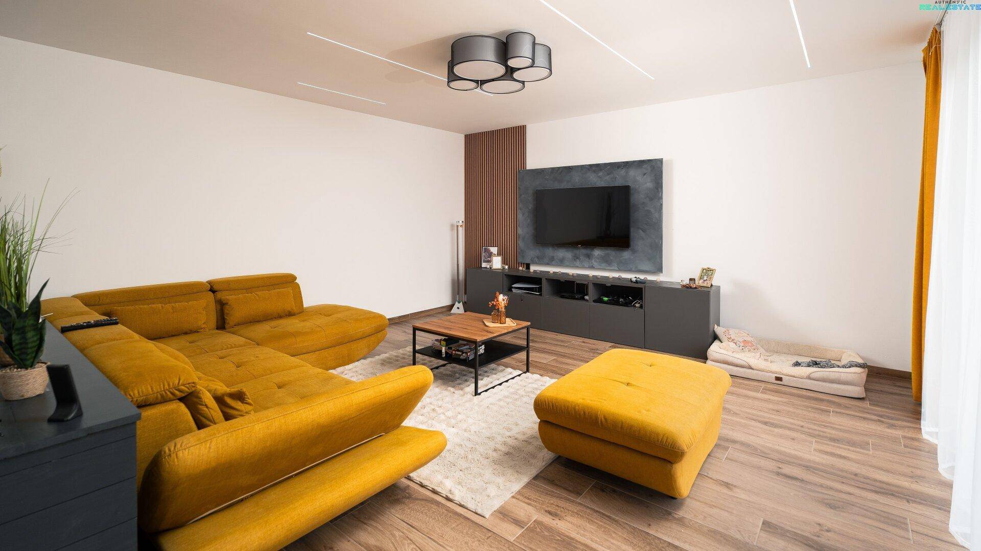 Gemütliches Wohnzimmer mit großem gelbem Ecksofa und modernem TV-Bereich, ideal zum Entspannen.
