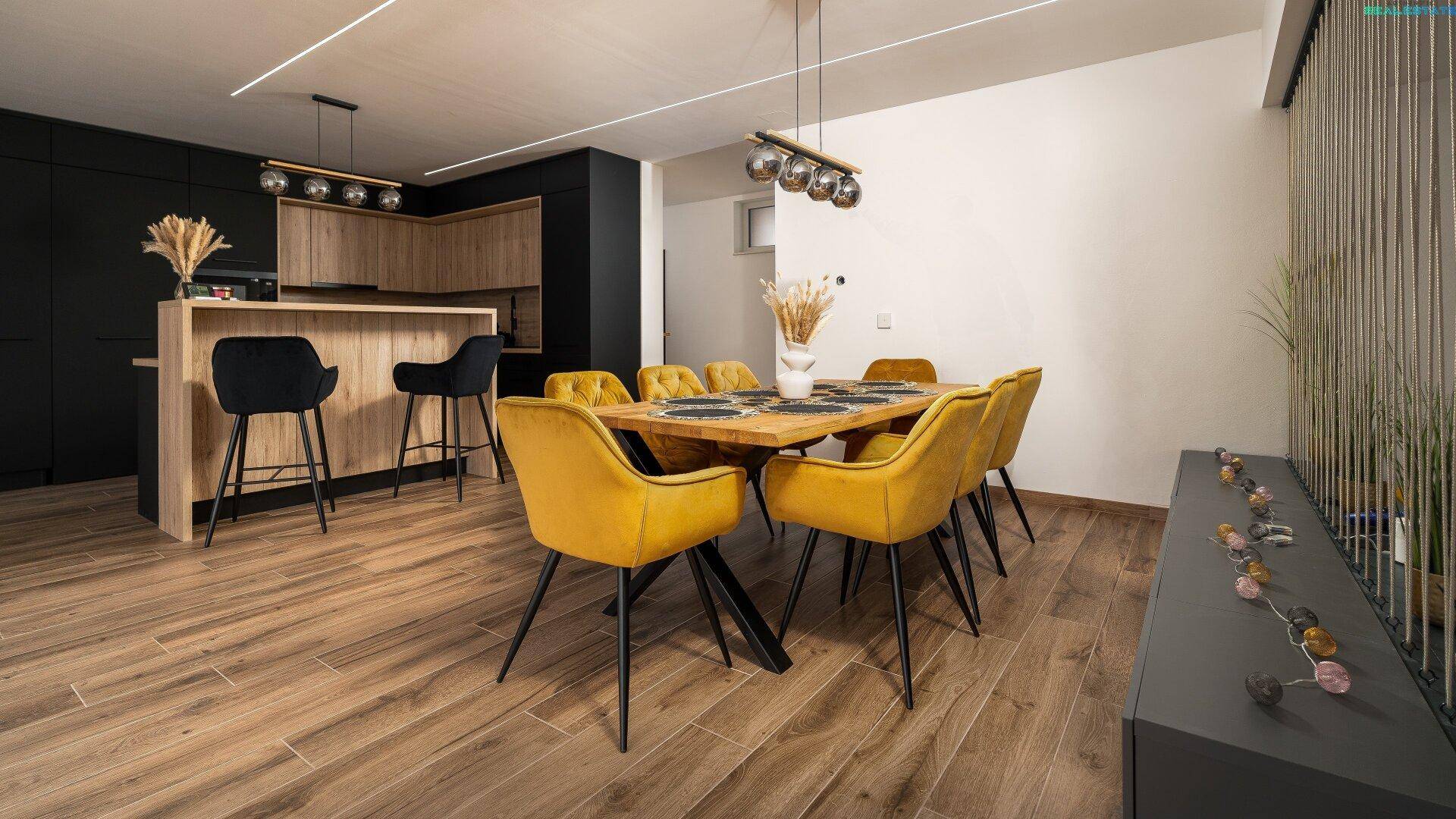Moderner Essbereich mit Holztisch, gelben Stühlen und offener Küche im Hintergrund, ideal für Geselligkeit.