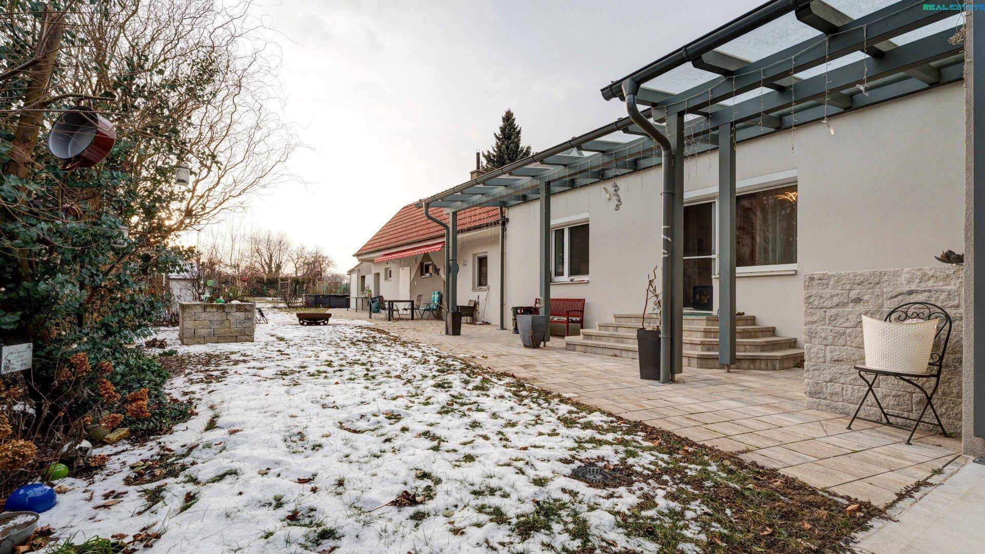 Großer Garten mit Terrasse, Überdachung und Sitzgelegenheiten, teilweise schneebedeckt.
