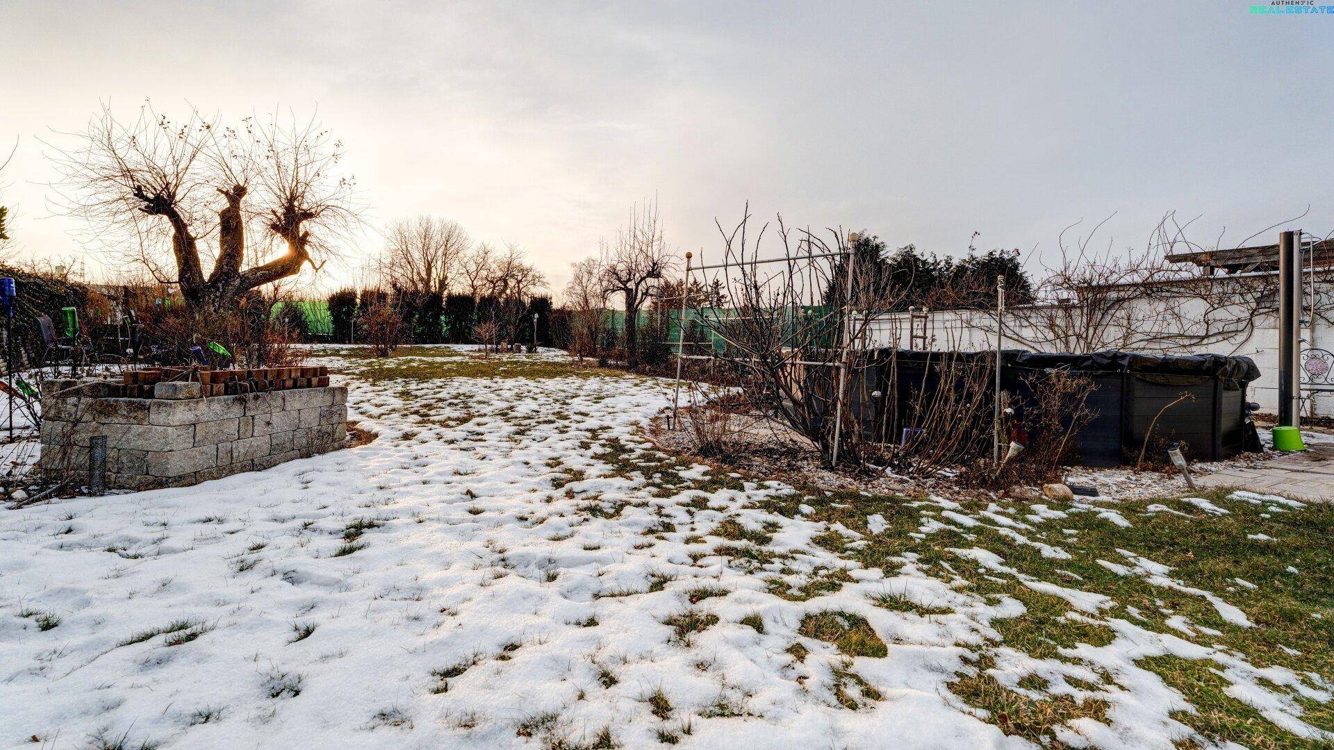 Weitläufiger Gartenbereich mit Rasenfläche, Bäumen und einem kleinen Pool, teilweise schneebedeckt.