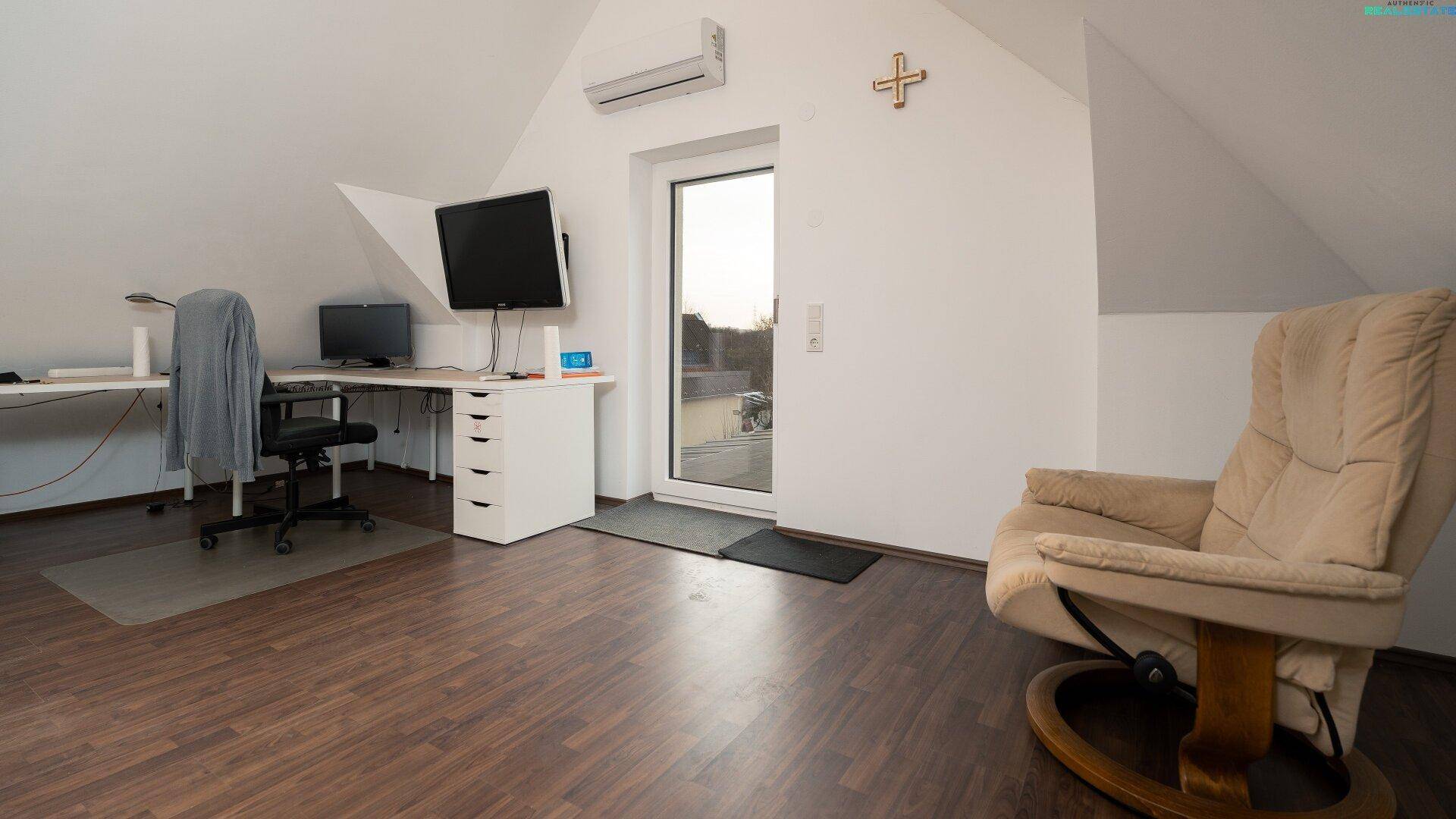 Helles Dachgeschoss-Büro mit Schreibtisch, Sessel und Zugang zu einem kleinen Balkon.