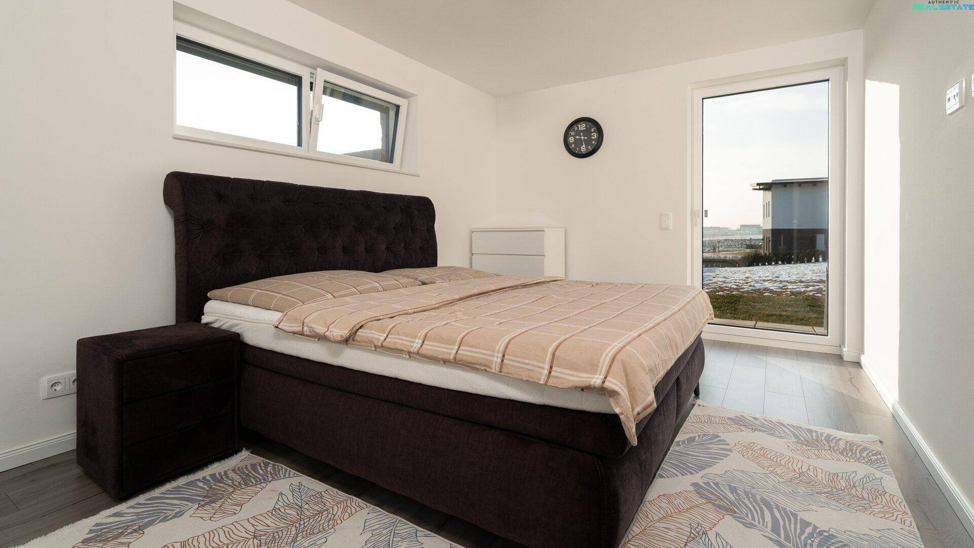 Gemütliches Schlafzimmer mit großem Bett, Holzboden und Fenster mit Blick ins Grüne.