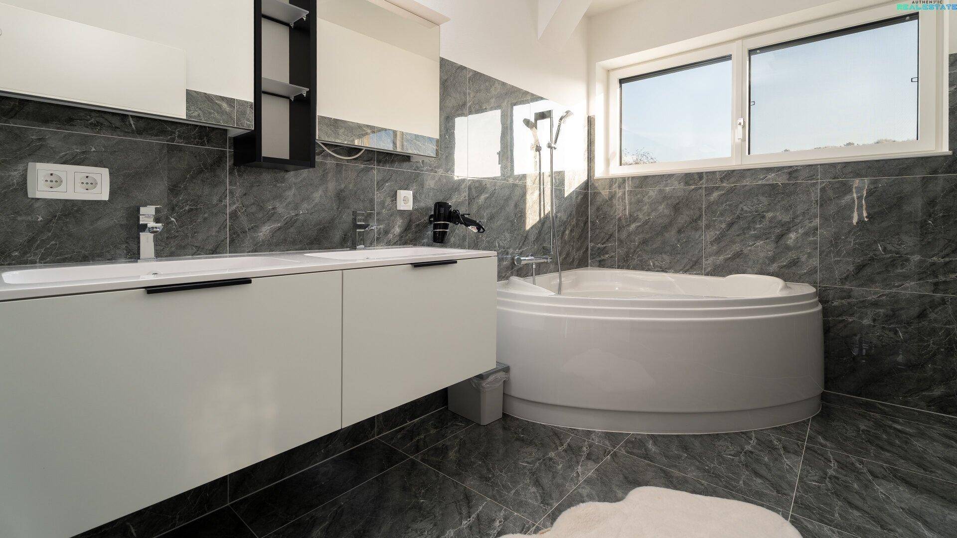 Modernes Badezimmer mit runder Badewanne, Doppelwaschbecken und dunklen Fliesen.