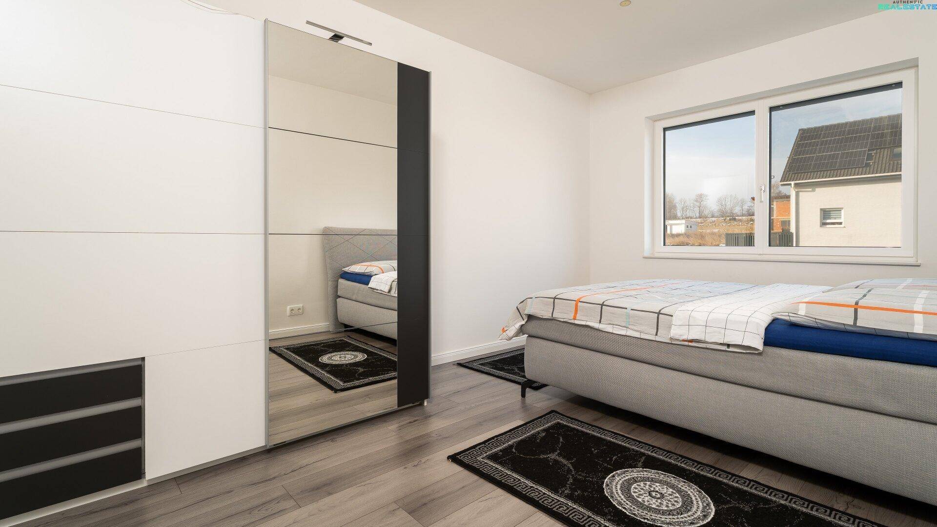 Schlafzimmer mit großem Bett, Spiegelschrank und Holzboden.
