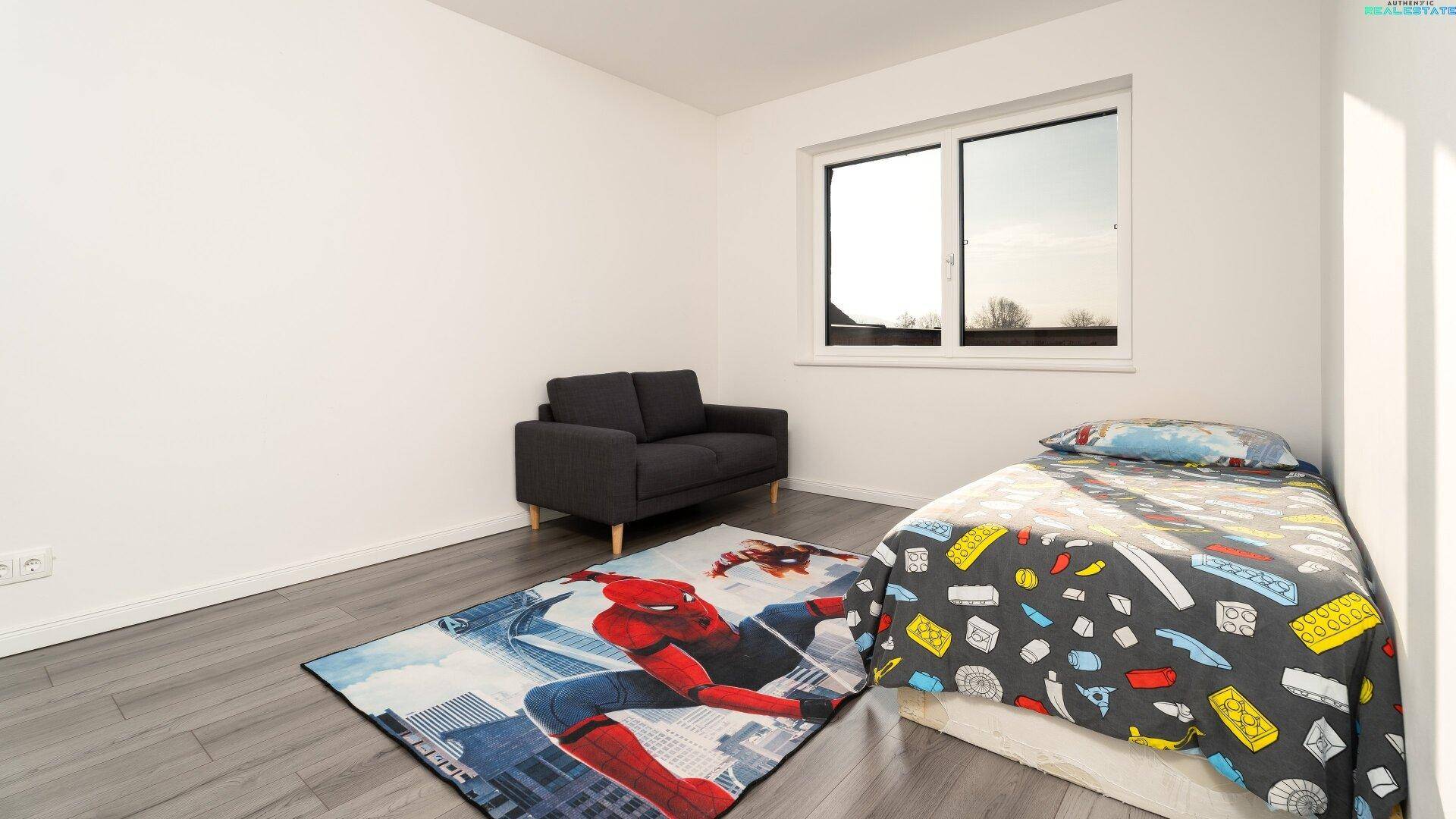 Kinderzimmer mit Einzelbett, kleinem Sofa und farbenfrohem Spiderman-Teppich.
