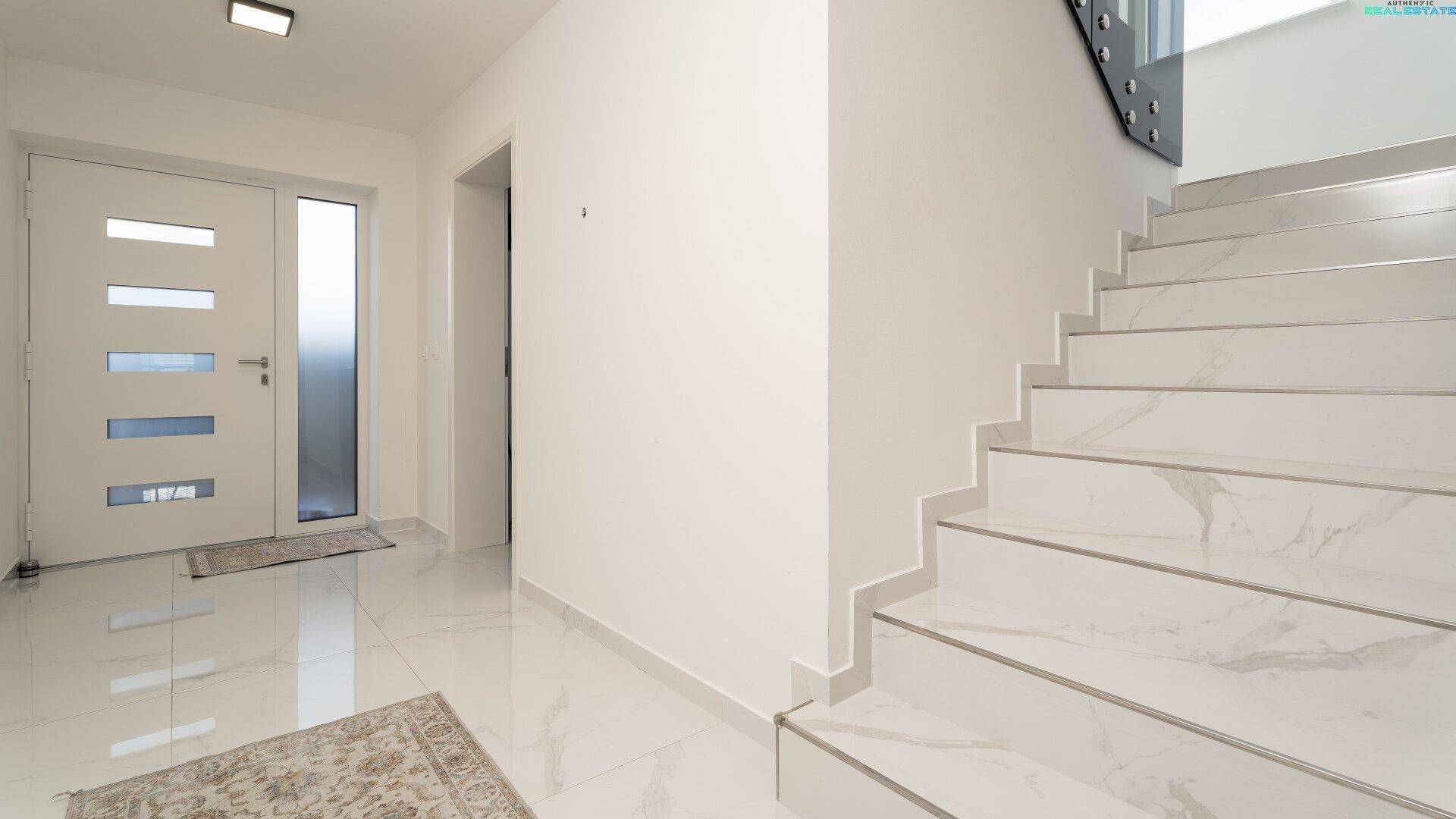Heller Eingangsbereich mit modernen Fliesen, Treppe und weißer Eingangstür.