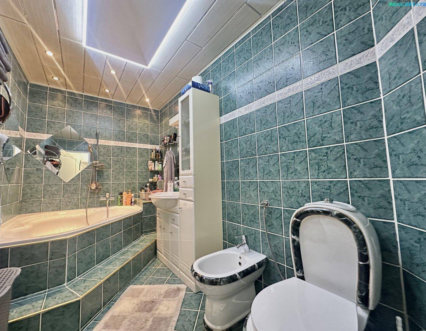 Badezimmer mit grünen Fliesen, Badewanne, Bidet und Toilette, ausgestattet mit Spiegelflächen.