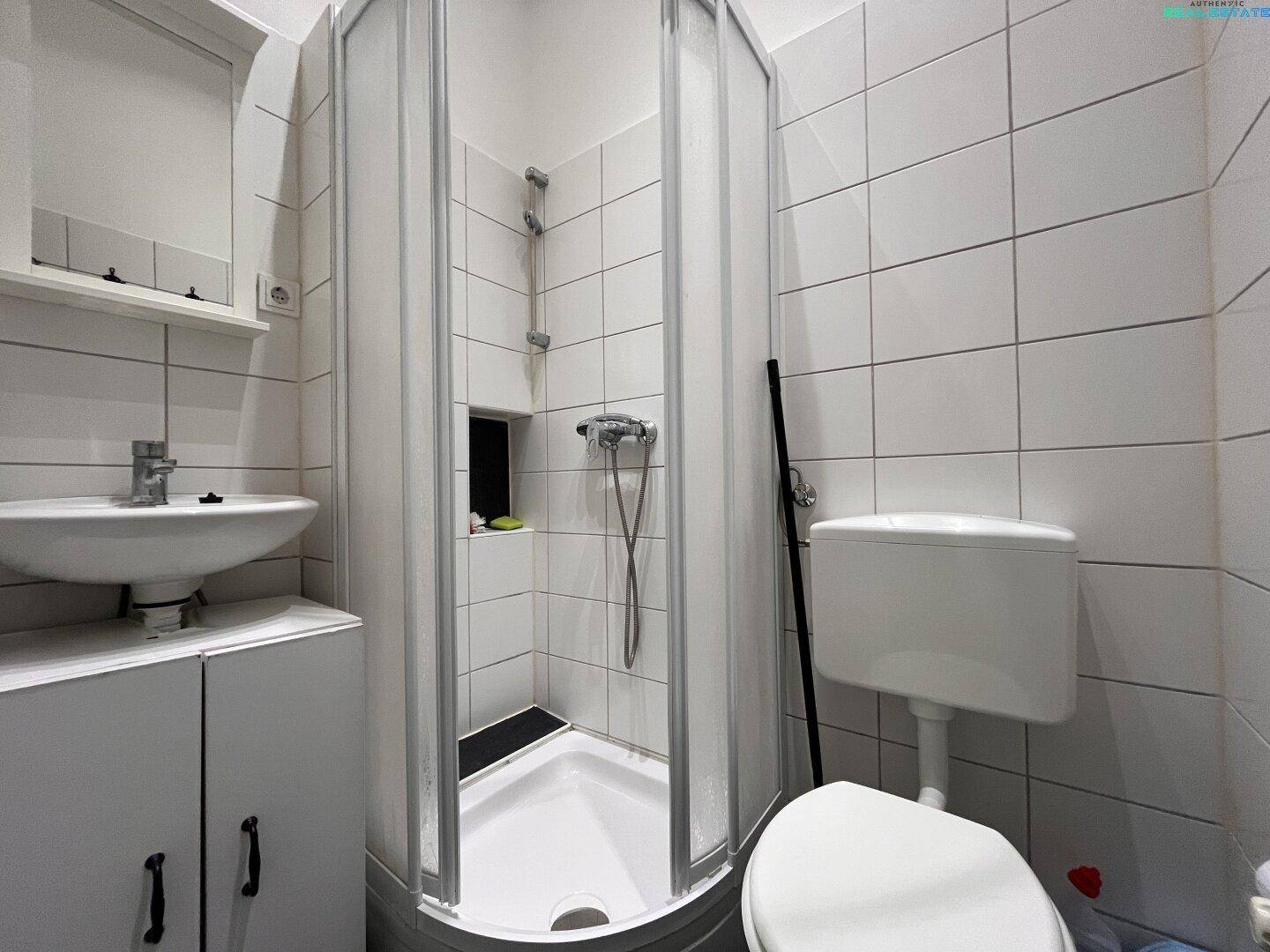 Kleines Badezimmer mit weiß gefliesten Wänden, Duschkabine und Waschbecken.