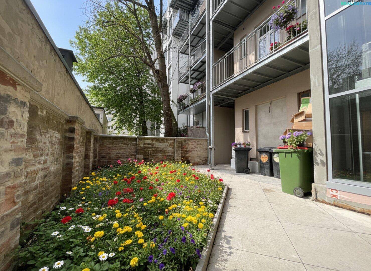 Bunter Gemeinschaftsgarten mit Blumenbeeten und Balkonen im Hintergrund.