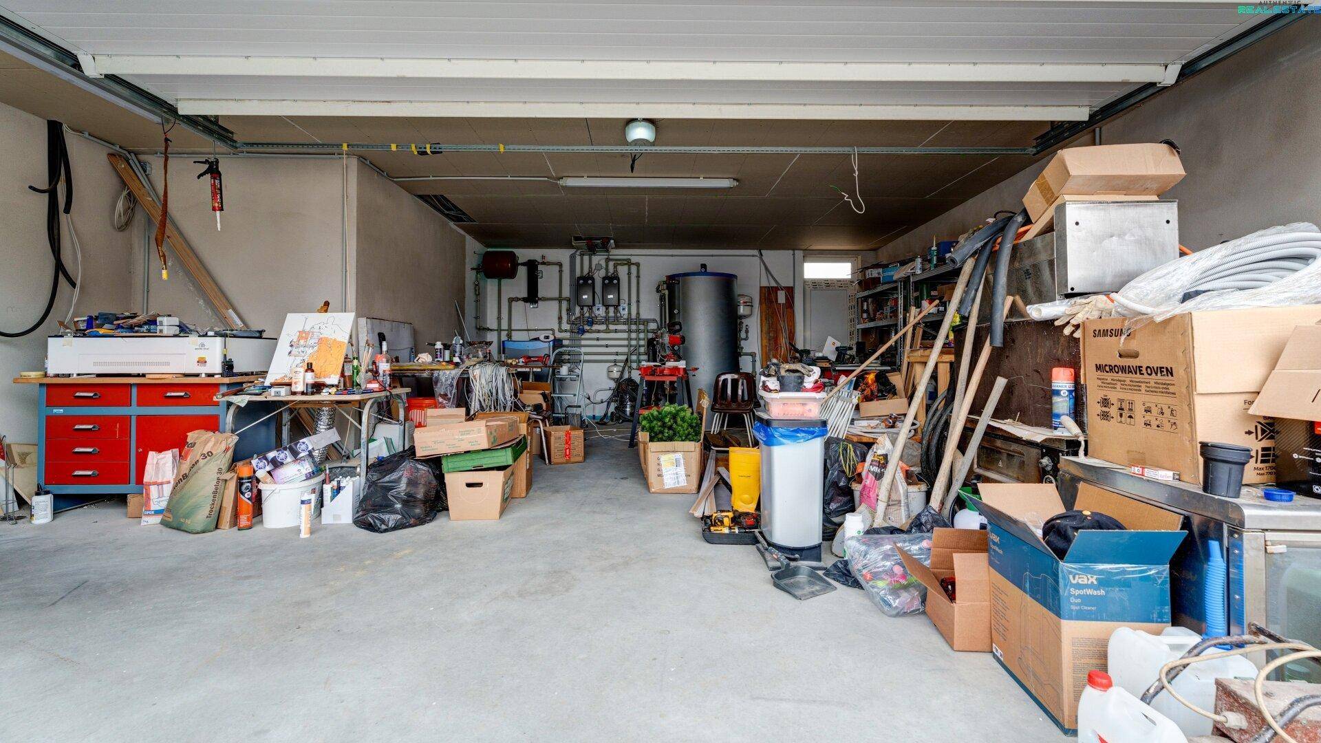 Geräumige Garage mit Betonboden, viel Stauraum und sichtbaren Versorgungsleitungen an der Rückwand.