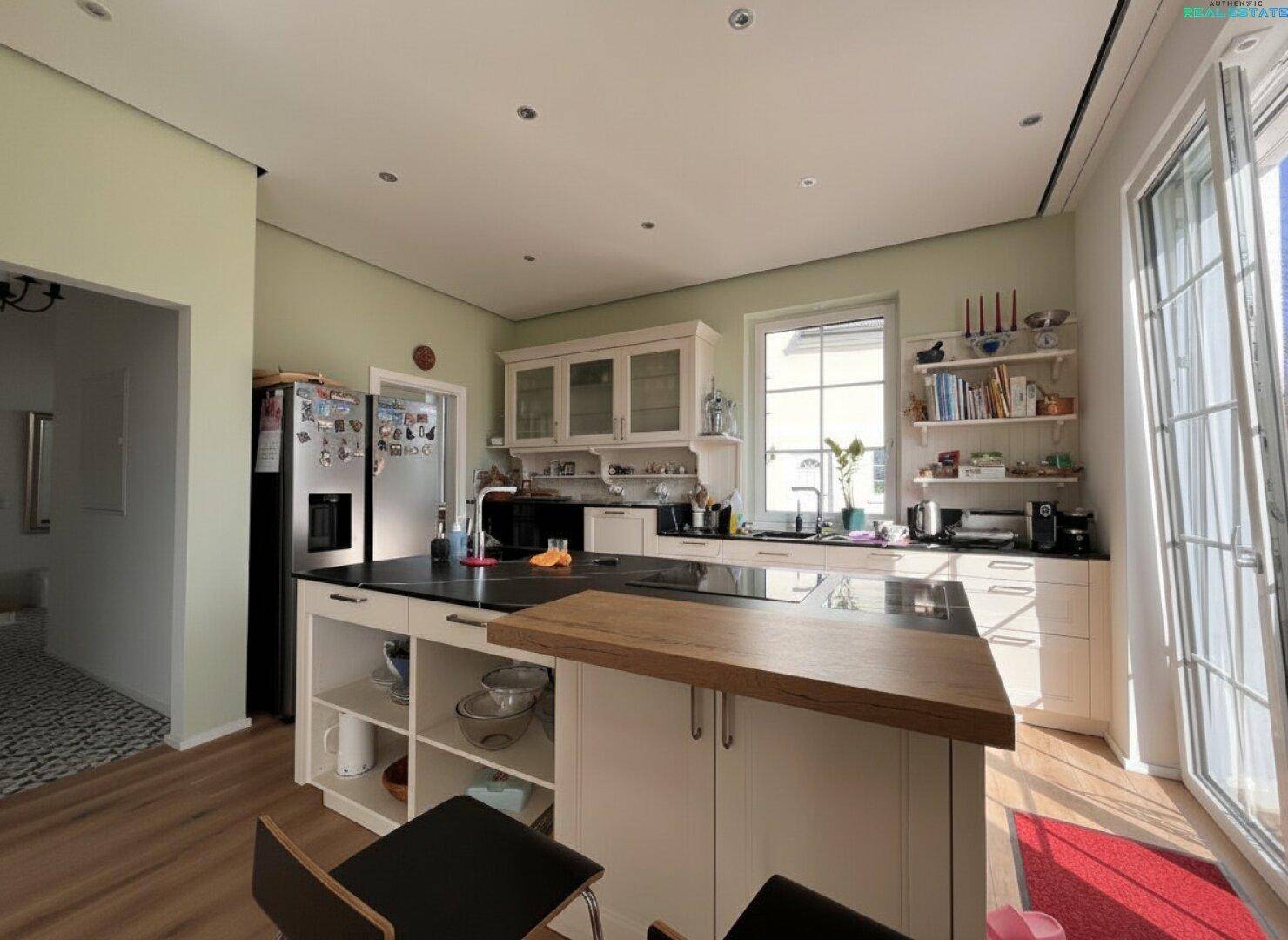 Helle Küche mit Kücheninsel, dunkler Arbeitsplatte, Holzboden und modernen Geräten.