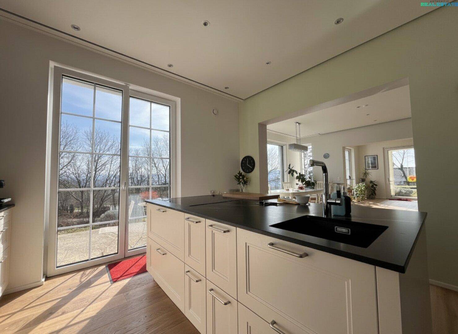 Moderne Küche mit Kücheninsel, Zugang zur Terrasse und großen Fenstern mit weitem Ausblick.