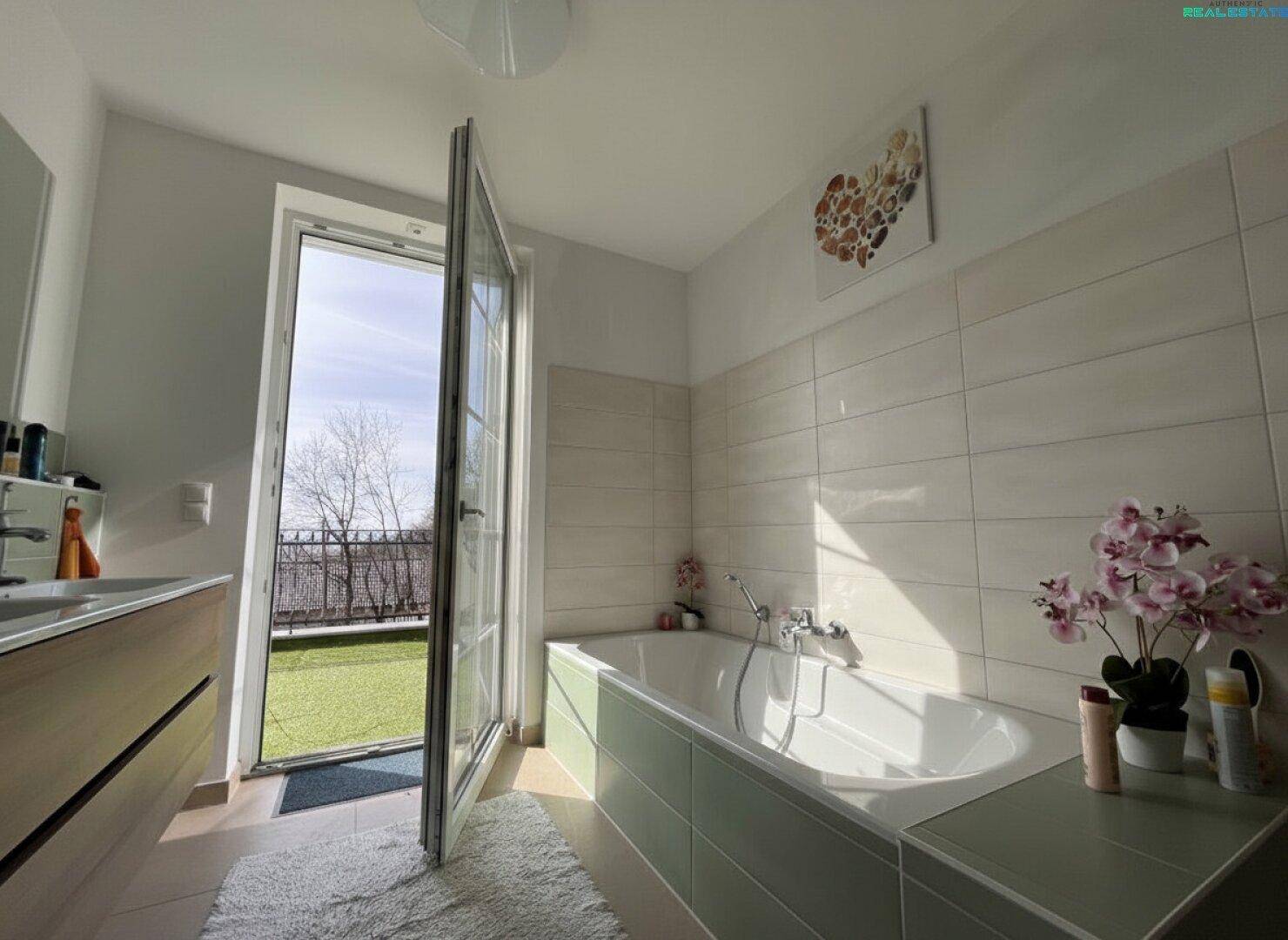 Helles Badezimmer mit Badewanne, modernen Fliesen und Zugang zu einem kleinen Balkon.